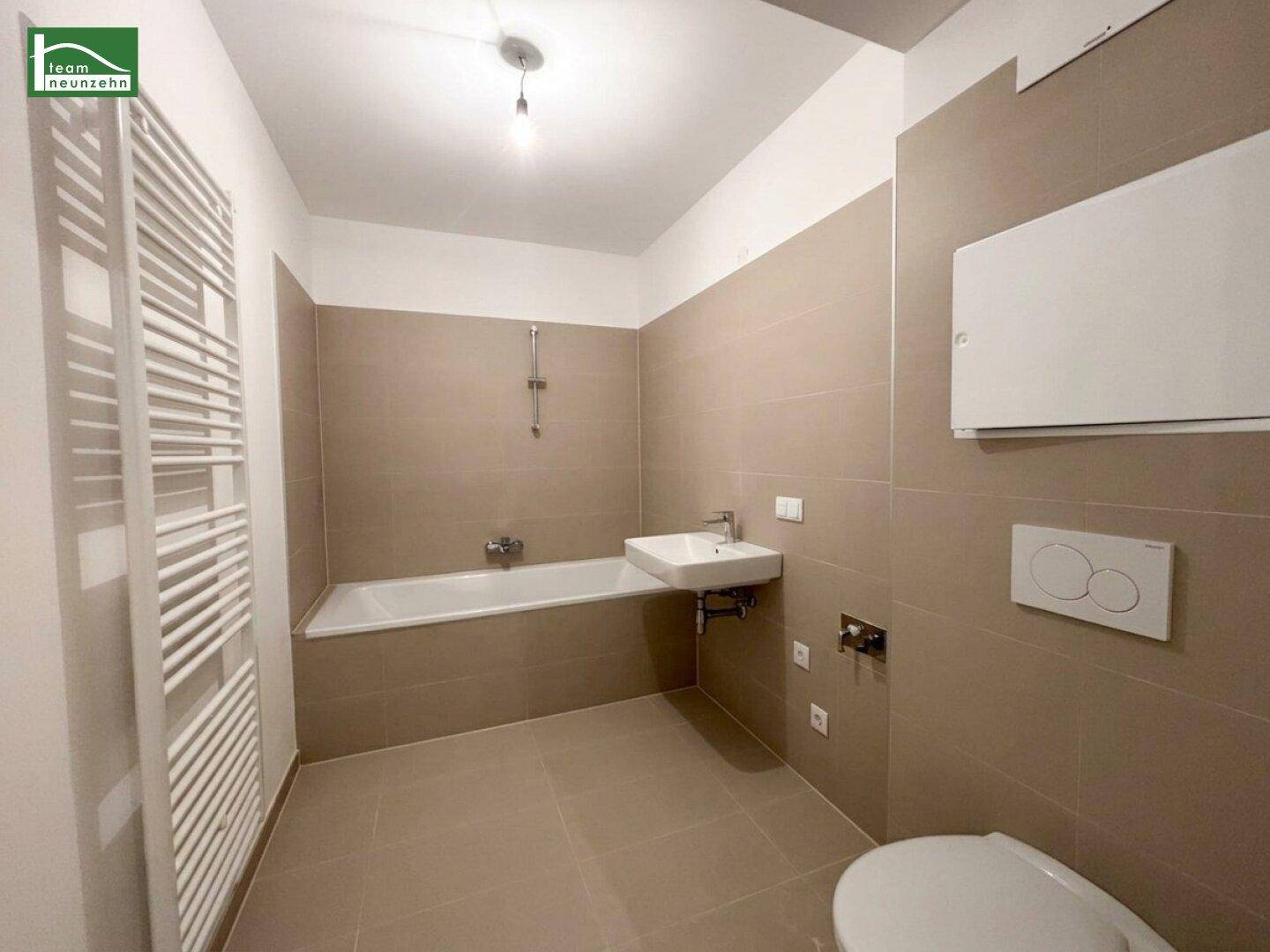 Modernes Badezimmer mit beigefarbenen Fliesen, Badewanne, Waschbecken und beheiztem Handtuchhalter.