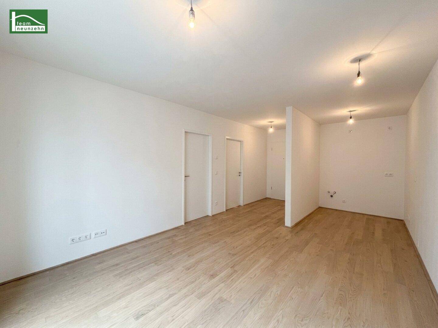 Geräumiges, leeres Zimmer mit hellem Holzboden und mehreren Türen in einem modernen Gebäude.