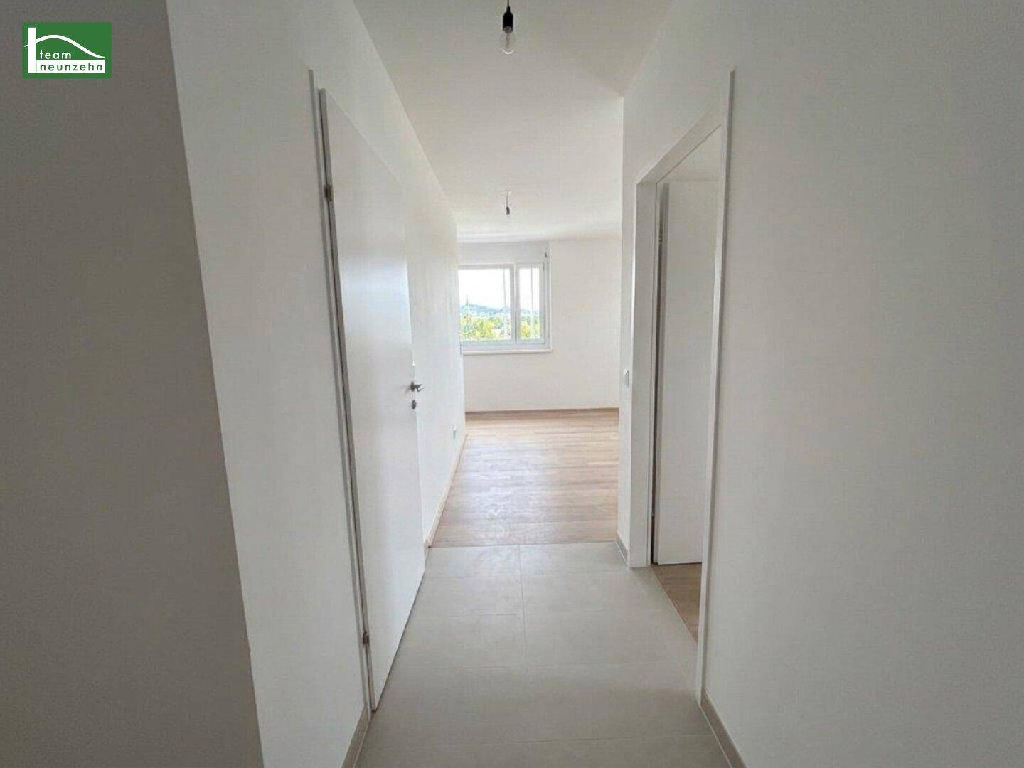Heller Flur mit Fliesenboden, der zu einem weiteren Zimmer mit Fenster führt.