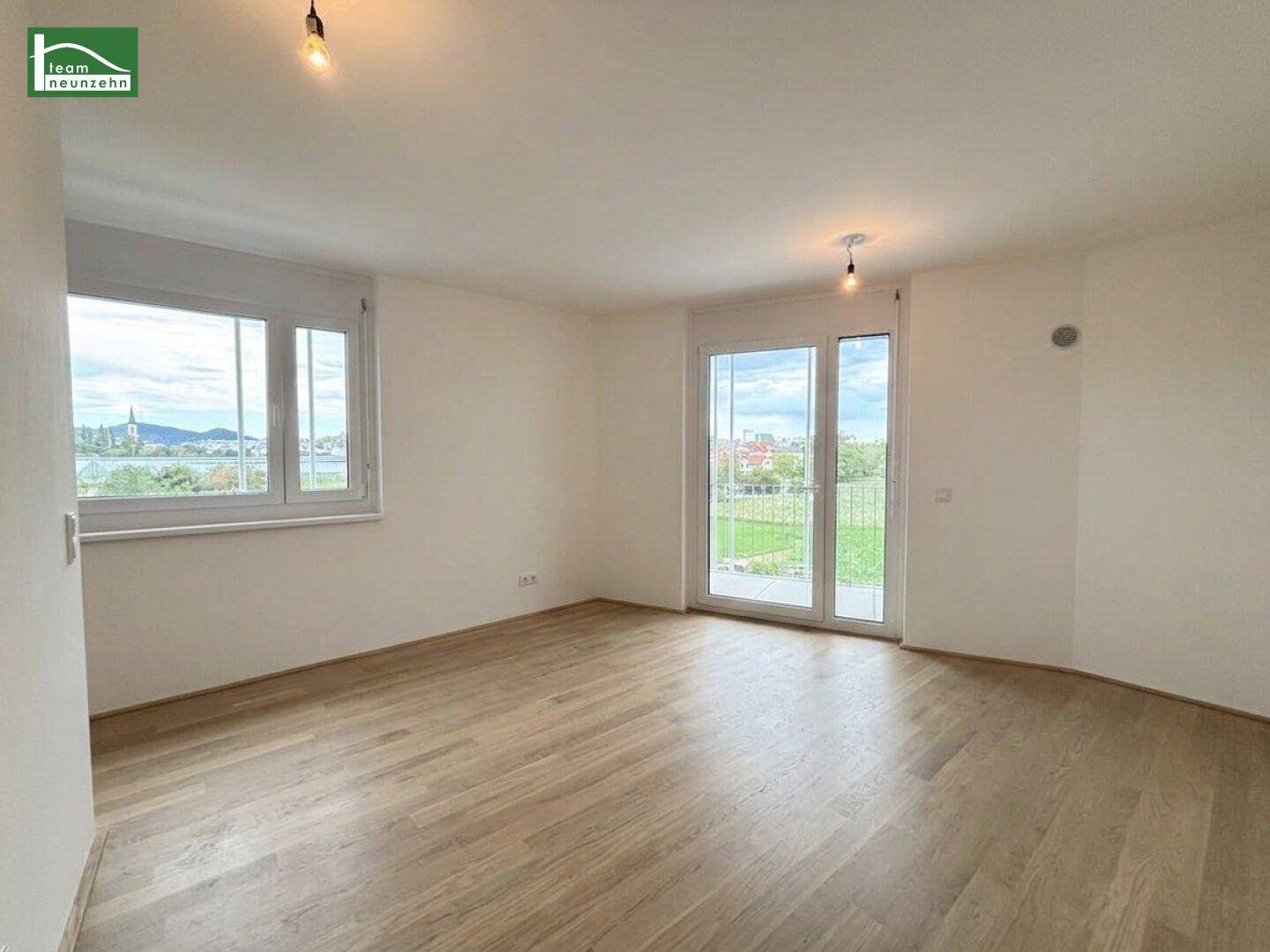 Helles Wohnzimmer mit Parkettboden, großen Fenstern und direktem Zugang zum Balkon.