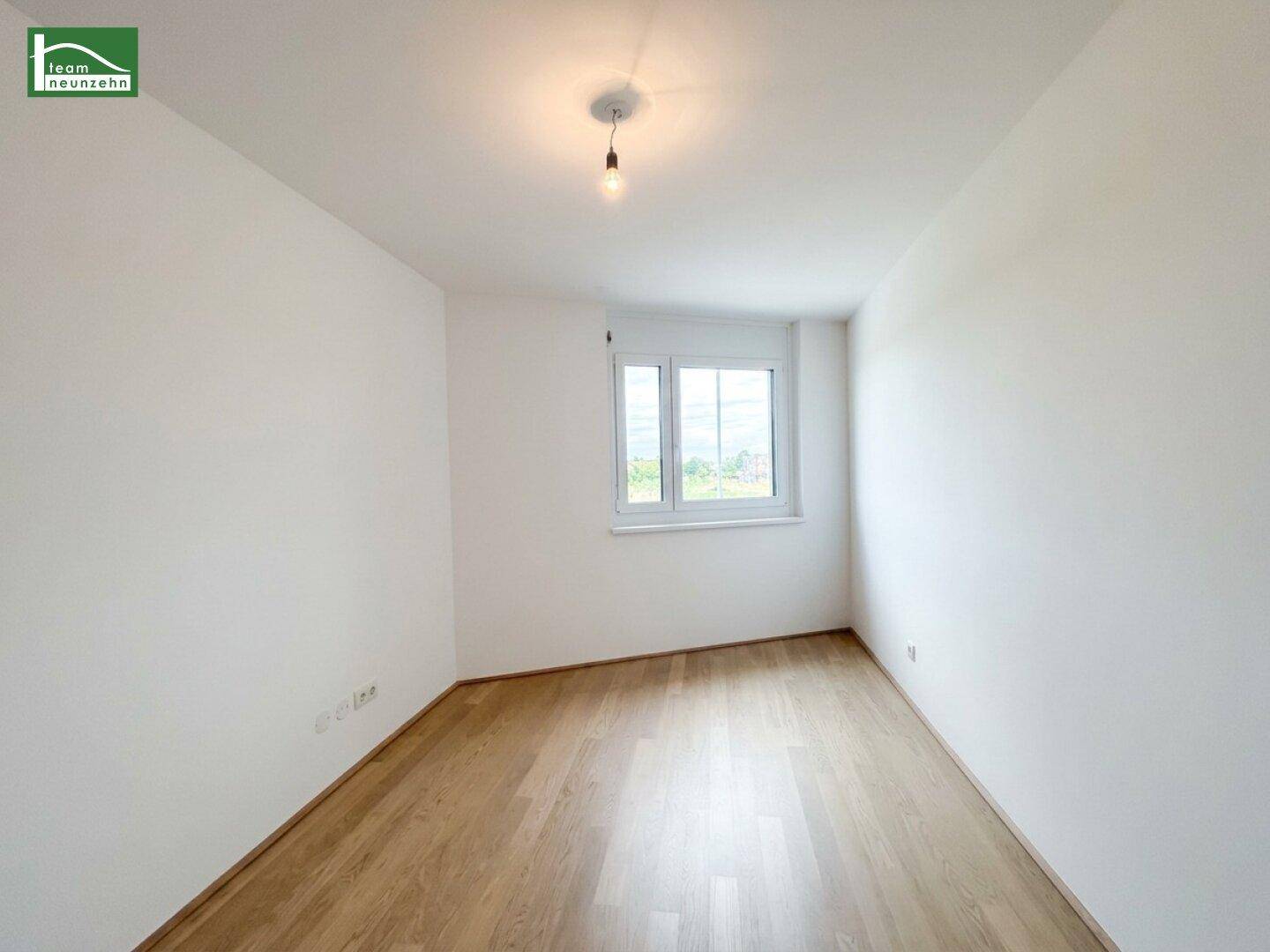 Leeres Schlafzimmer mit hellem Parkettboden und einem Fenster, das viel Tageslicht hereinlässt.