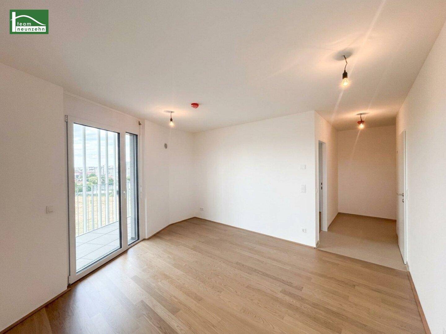 Geräumiges Zimmer mit hellem Holzboden und Zugang zu einem Flur, ideal für offenes Wohnen.