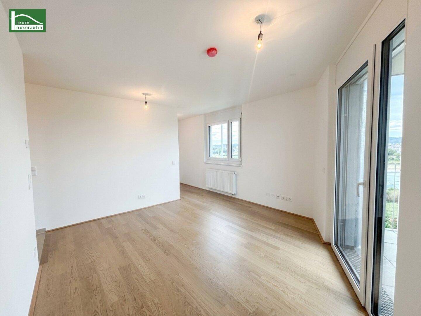 Lichtdurchfluteter Raum mit Holzboden, Heizkörper und Zugang zu einem Balkon, bietet vielseitige Nutzung.