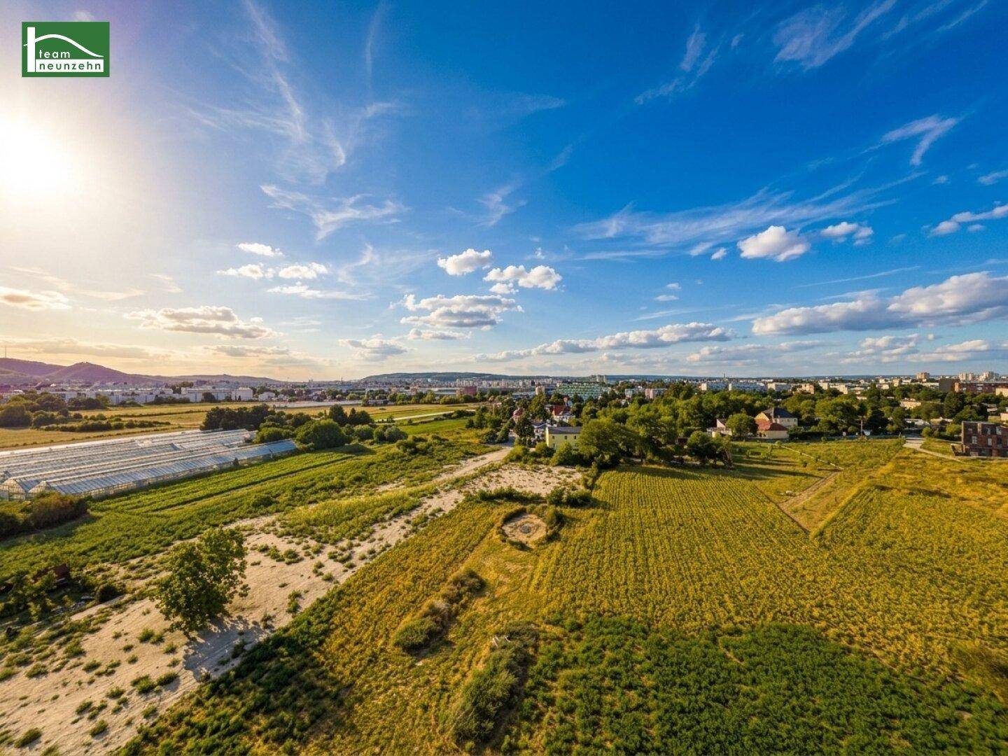 Weitläufige Landschaftsaufnahme mit Feldern, Bäumen und Siedlungen unter blauem Himmel.