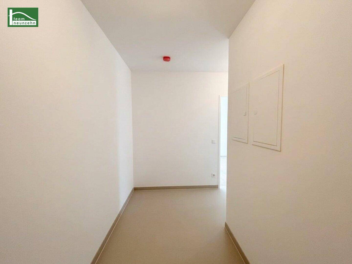Heller, schlichter Flur mit Fliesenboden und weißen Wänden, der zu weiteren Räumen führt.