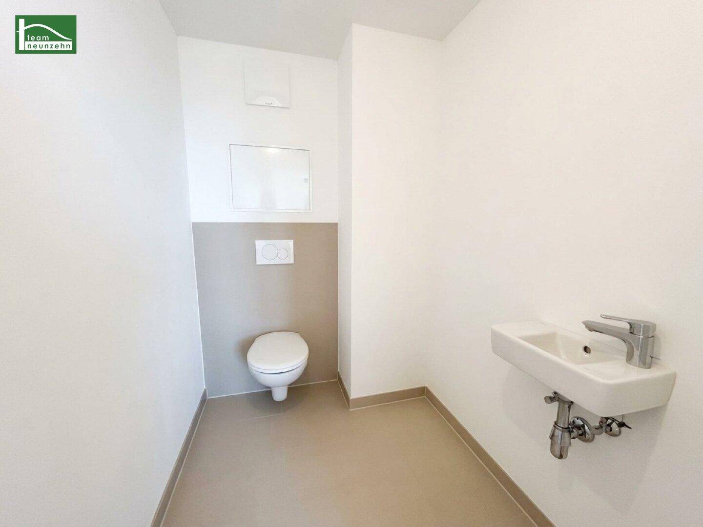 Kleines Gäste-WC mit wandhängender Toilette und kleinem Waschbecken, in hellen Farbtönen gehalten.