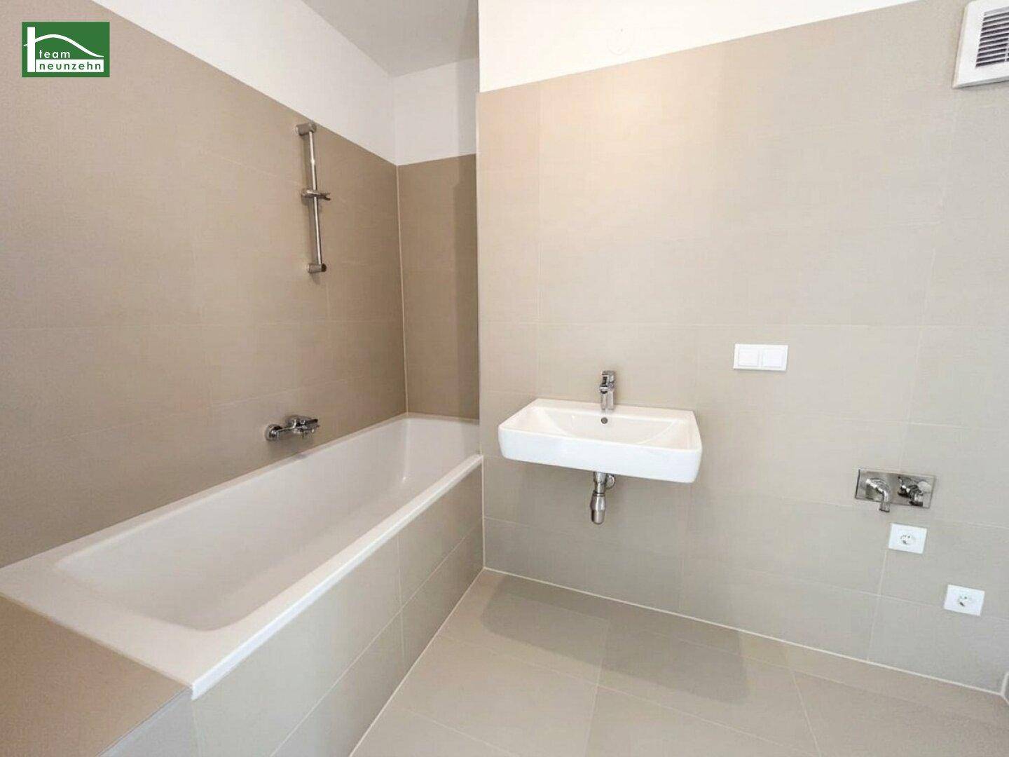 Modernes Badezimmer mit Badewanne, Einzelwaschbecken und hellbeigen Fliesen an Wänden und Boden.