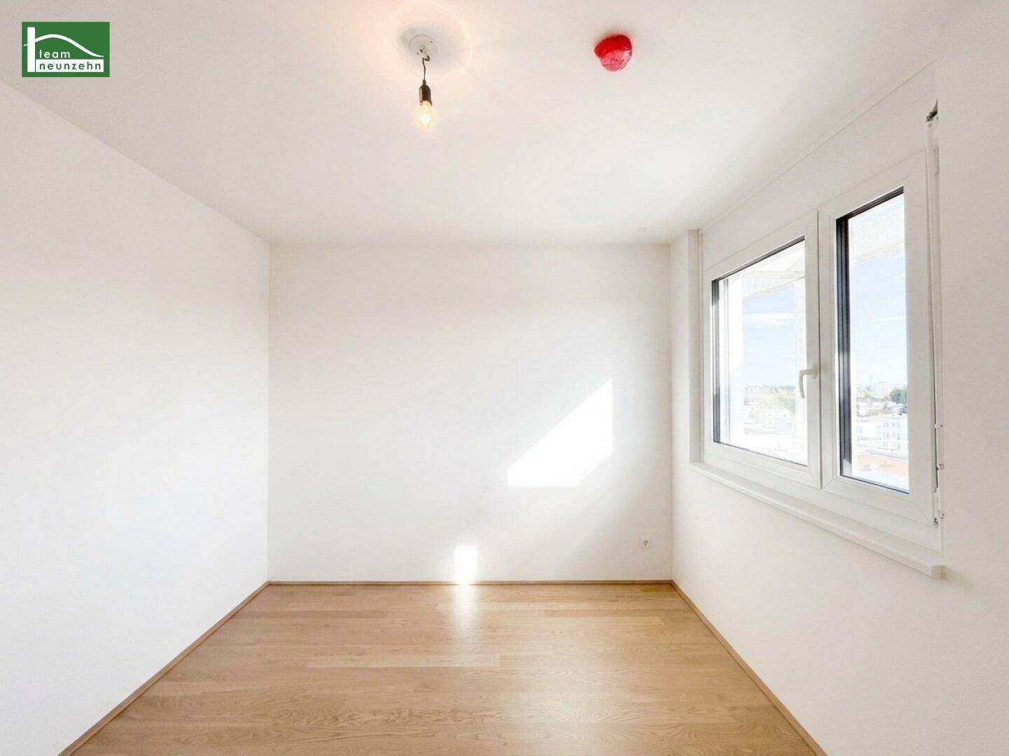Helles, leeres Zimmer mit Holzboden und großem Fenster, ideal als Schlaf- oder Arbeitszimmer.
