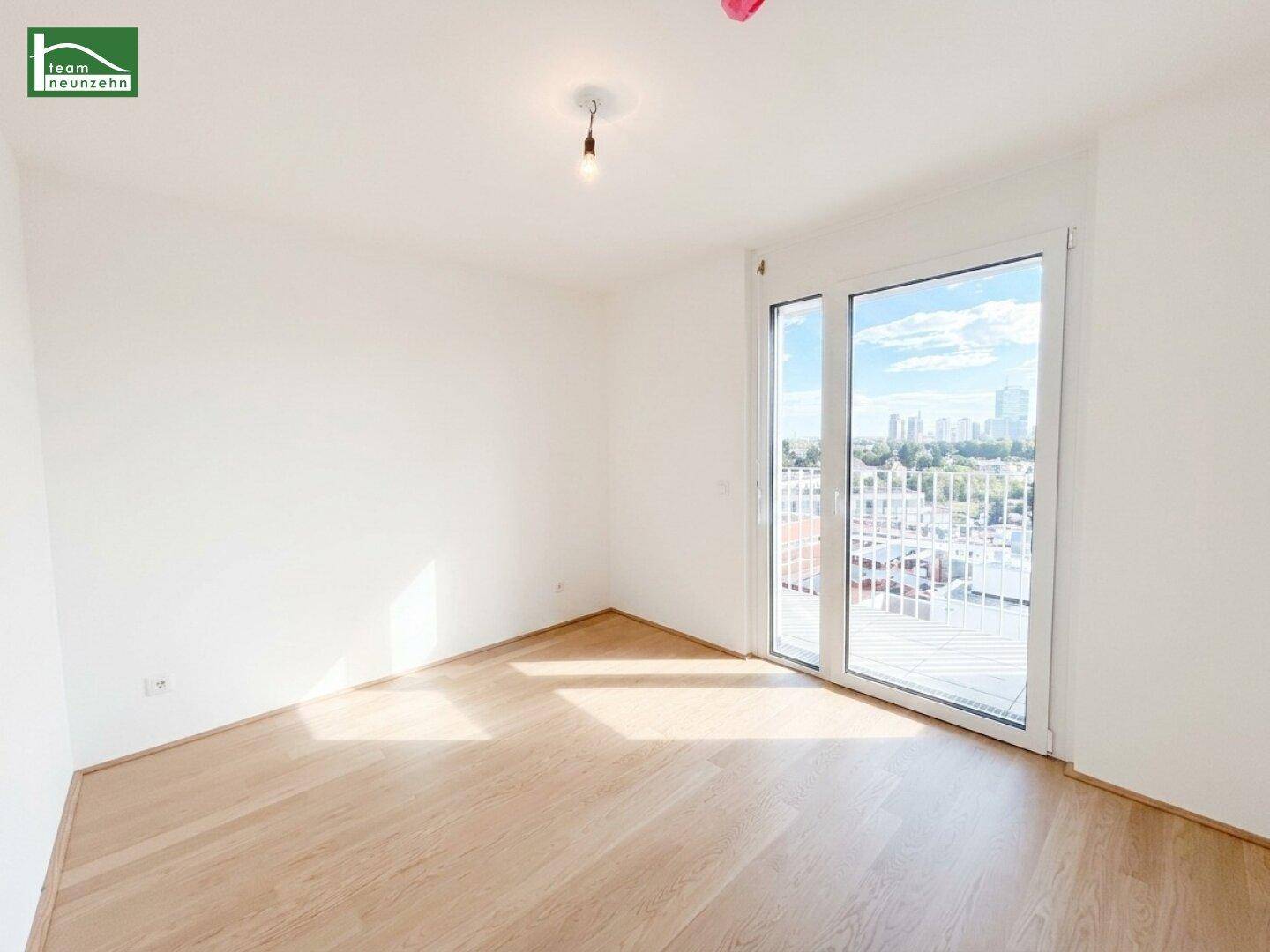 Geräumiges, helles Zimmer mit Holzboden und Zugang zu einem Außenbereich durch eine Glastür.