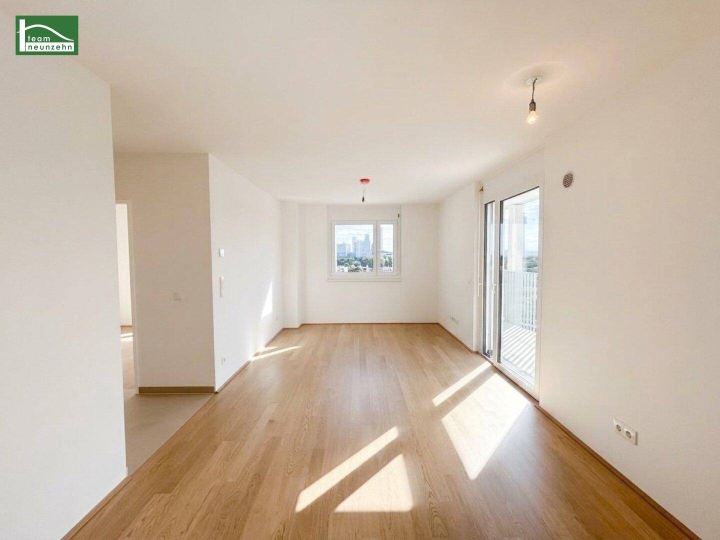 Heller, leerer Wohnraum mit hellem Holzparkett, weißen Wänden und Zugang zu einem Balkon.