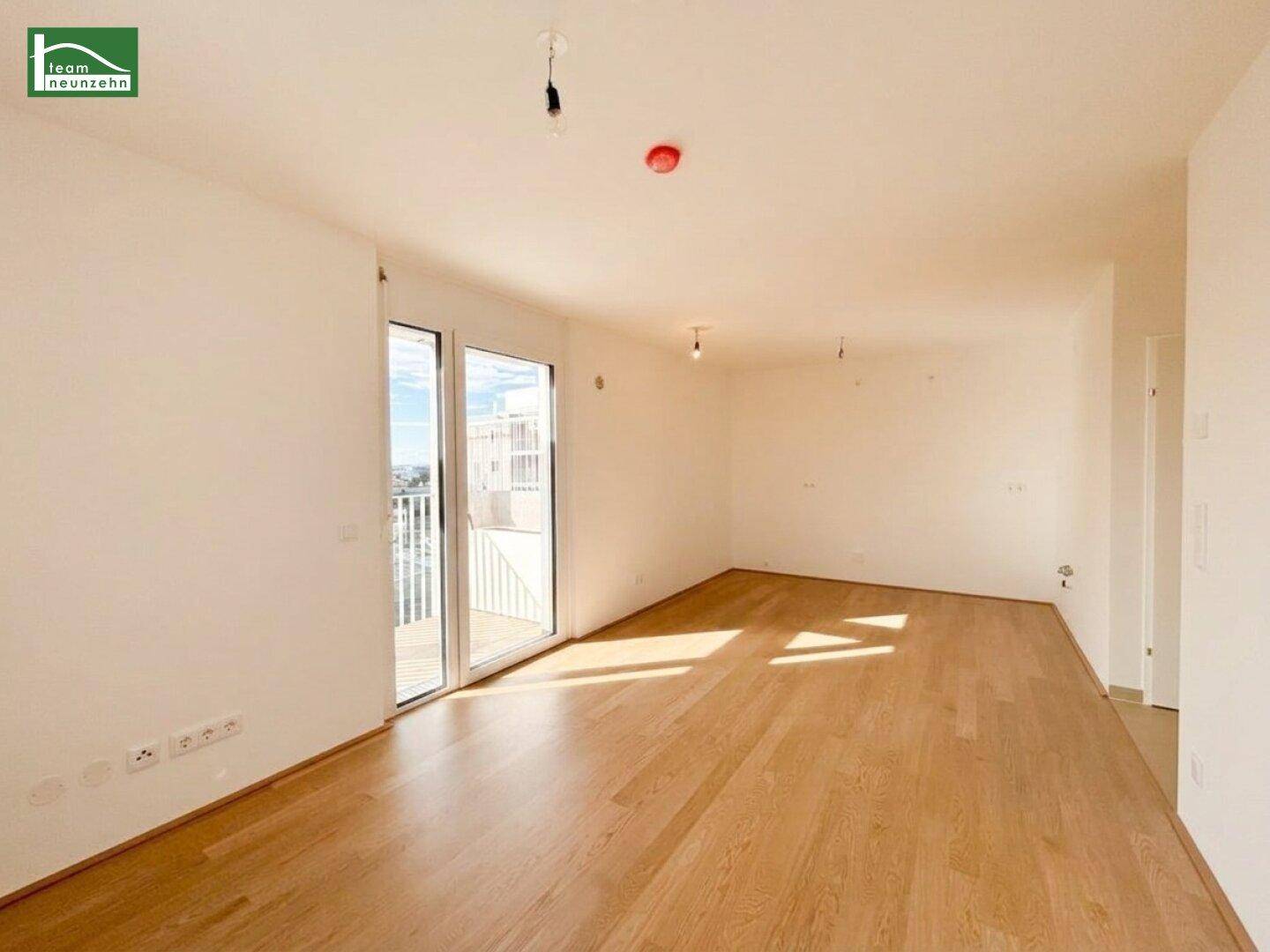 Lichtdurchfluteter Wohnbereich mit Holzboden und großer Glastür, die auf einen Außenbereich führt.