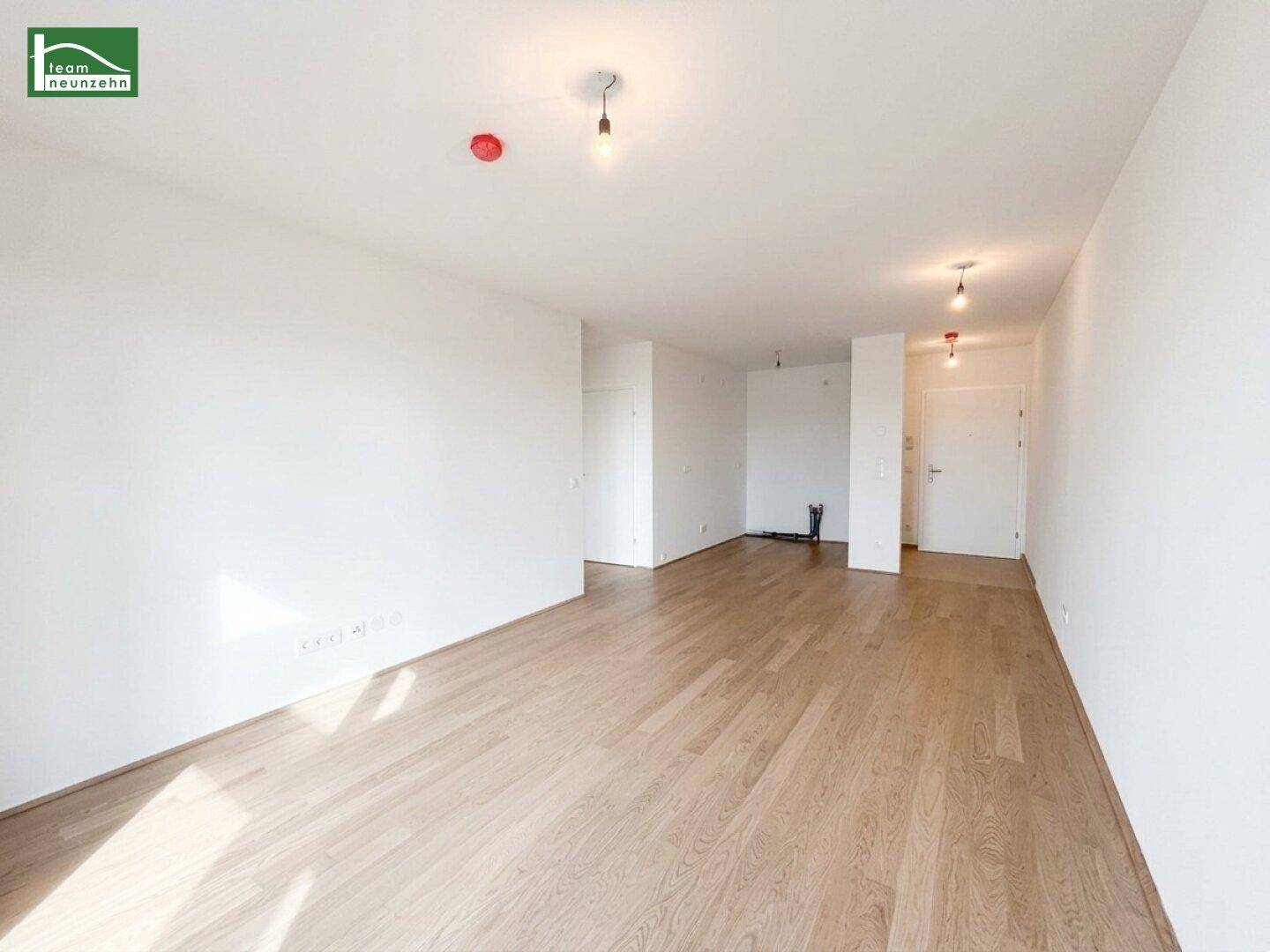 Heller, leerer Raum mit Holzfußboden und Zugang zu weiteren Zimmern.