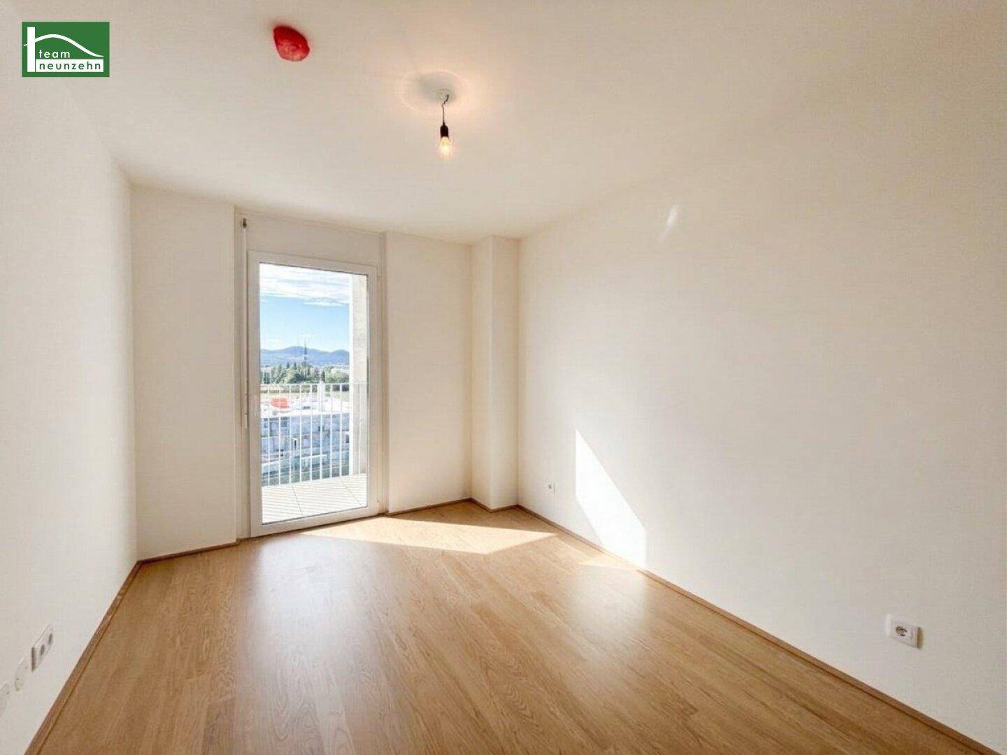 Helles, leeres Schlafzimmer mit Holzfußboden und direktem Zugang zum Balkon.