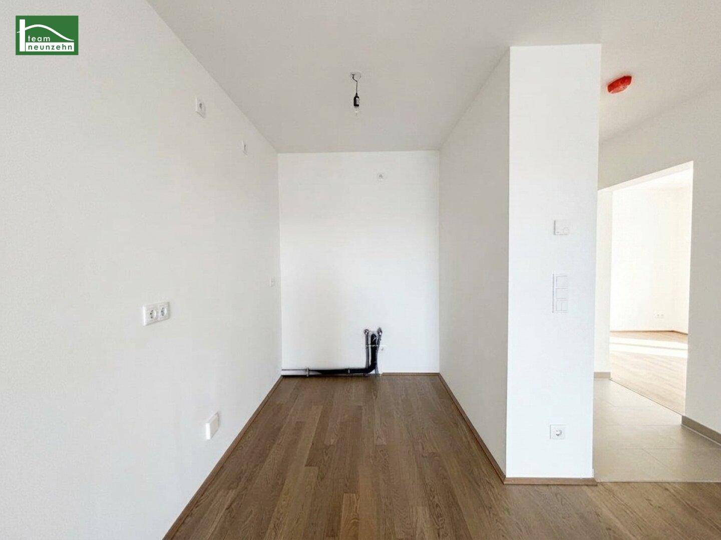 Leerer Küchenbereich mit Anschlüssen für eine Einbauküche und Holzfußboden.
