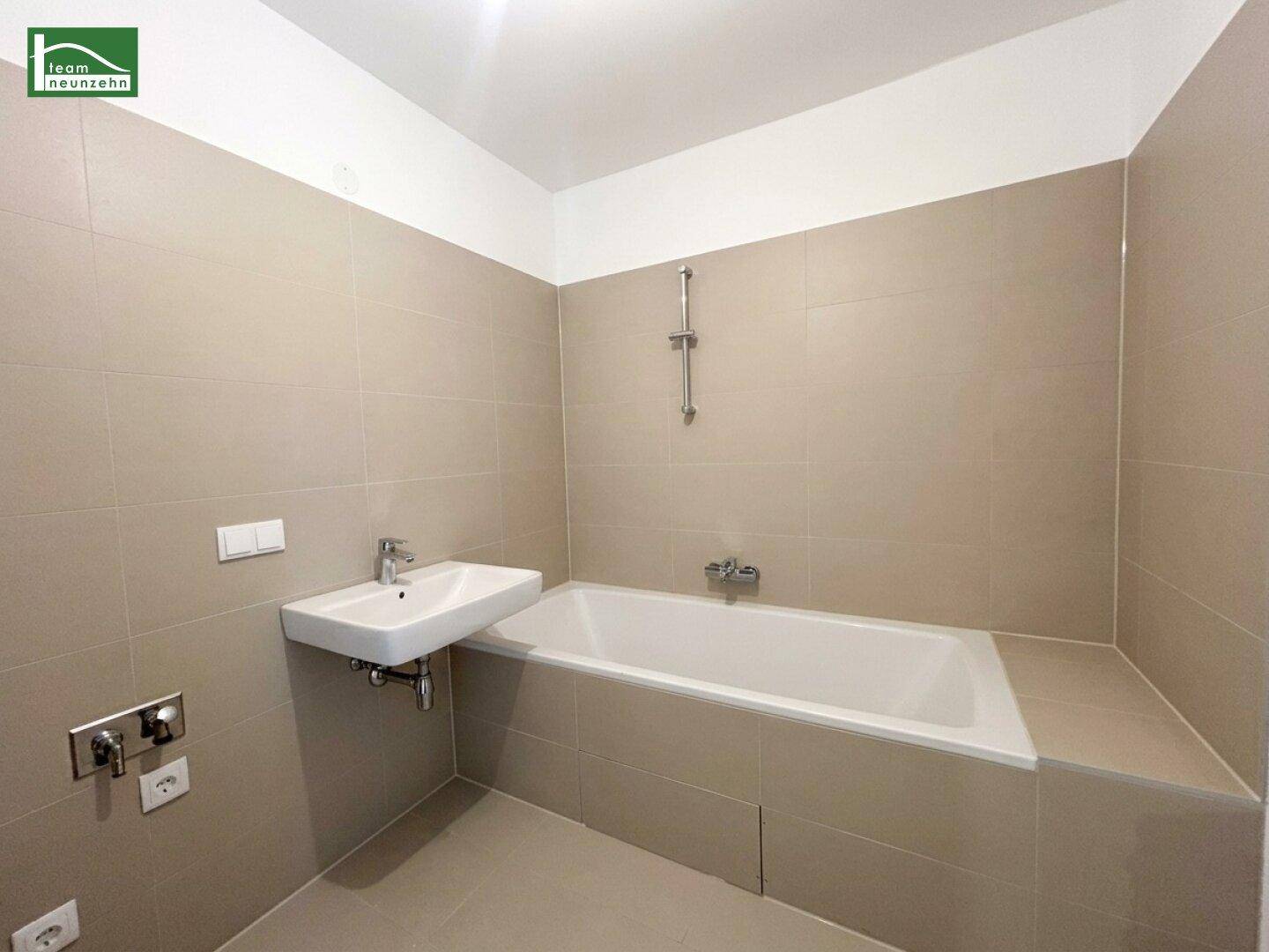 Modernes Badezimmer mit beigefarbenen Fliesen, Badewanne und einem einzelnen Waschbecken.