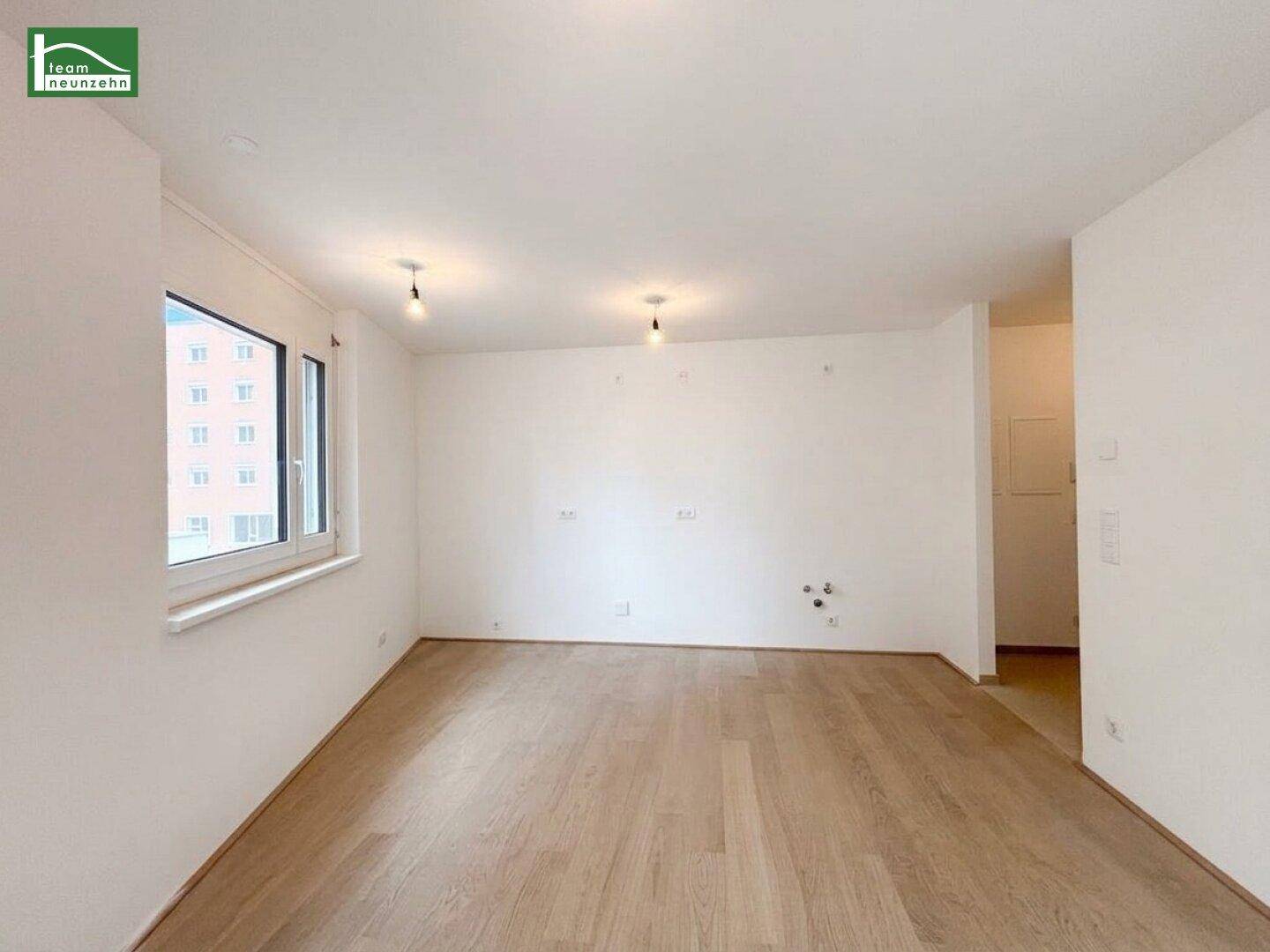 Geräumiges, leeres Zimmer mit hellem Holzboden und einem großen Fenster, bereit zur Einrichtung.