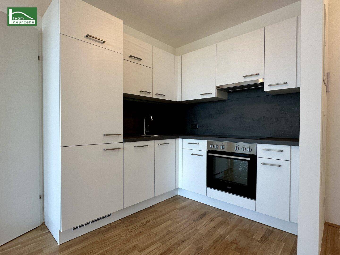 Moderne Einbauküche mit weißen Hochglanzfronten, dunkler Arbeitsplatte und integrierten Geräten.
