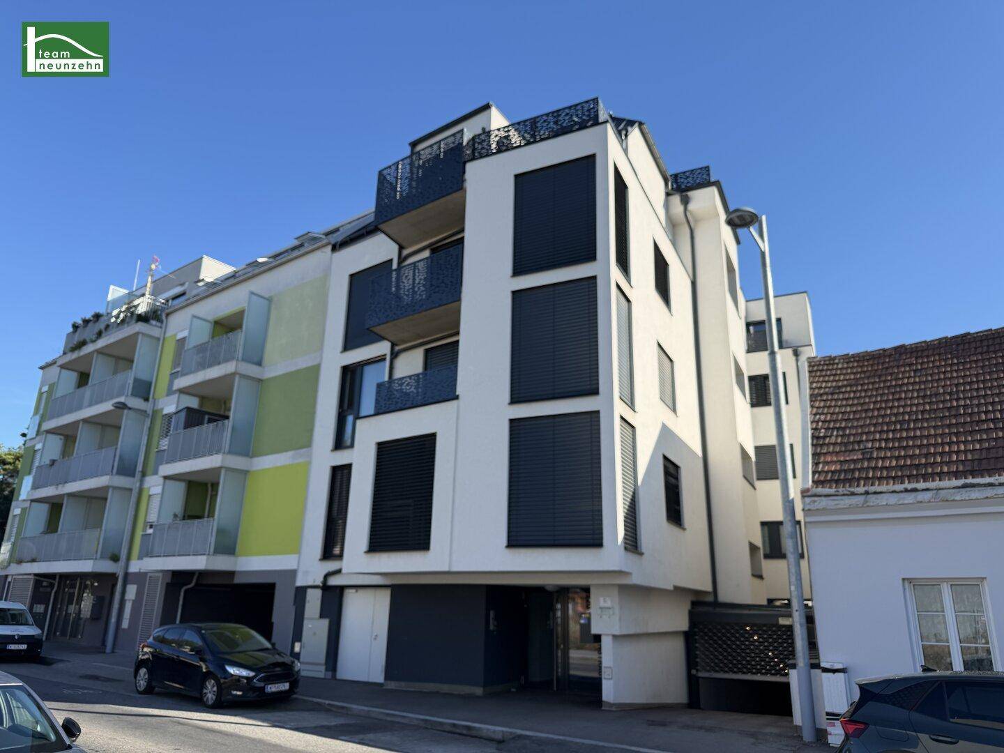Moderne Wohnanlage mit weißer Fassade, Balkonen und großen Fenstern an einem sonnigen Tag.