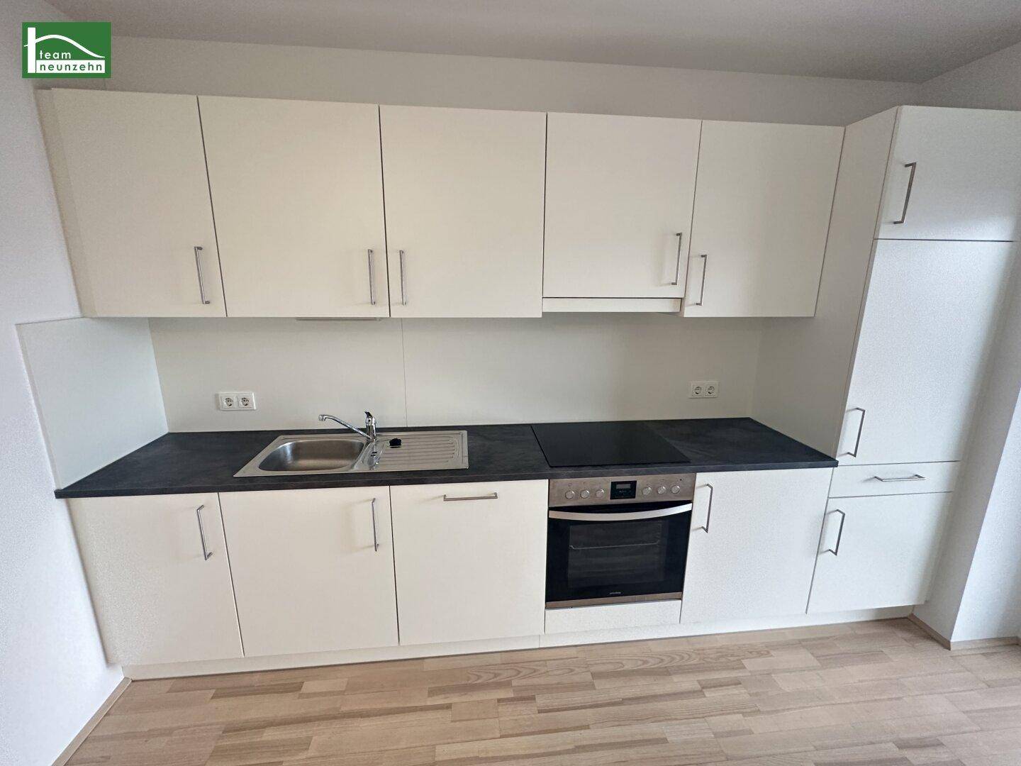 Moderne Einbauküche mit weißen Schränken, dunkler Arbeitsplatte und integrierten Geräten.
