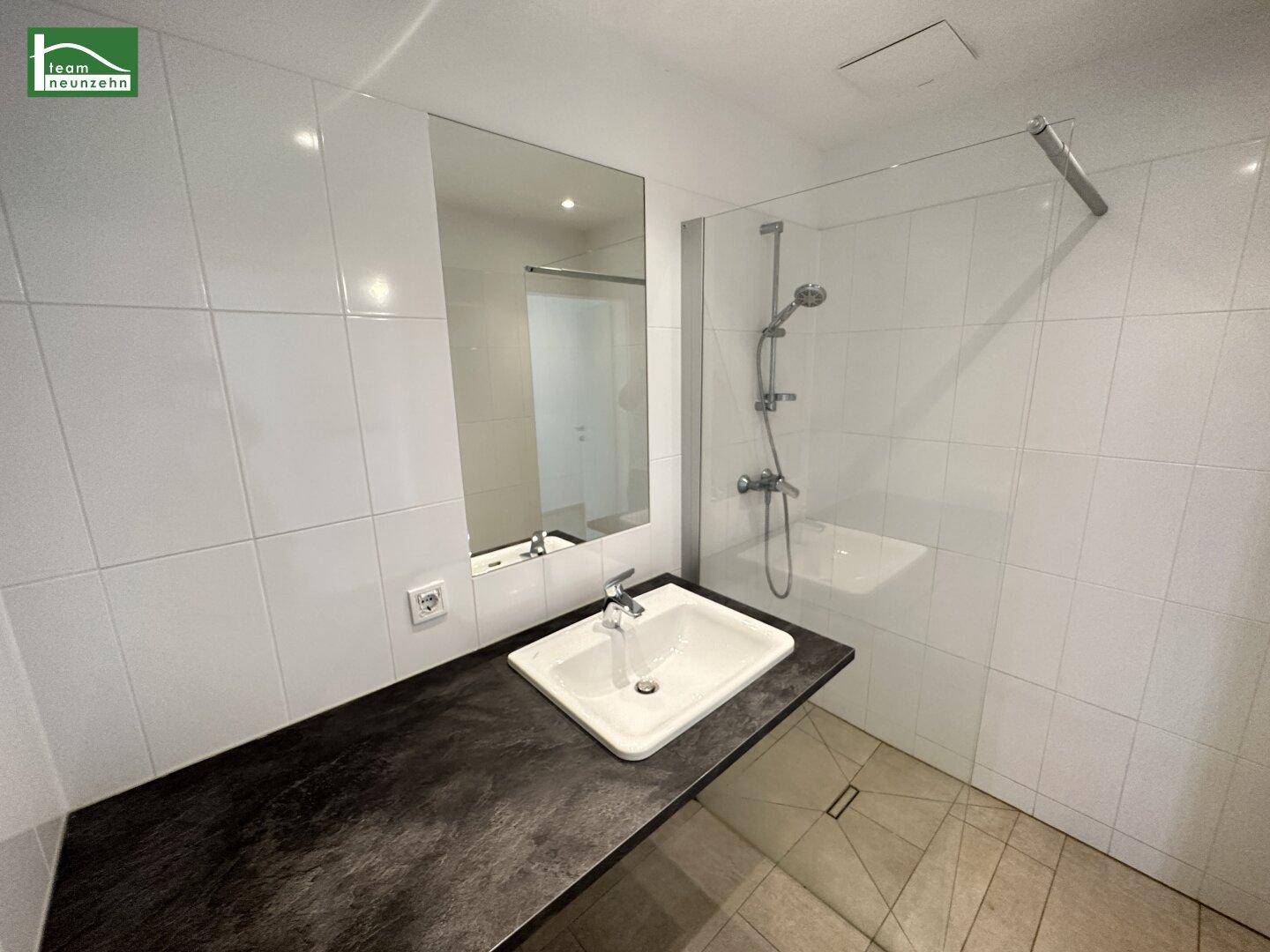 Modernes Badezimmer mit weißen Fliesen, großem Spiegel und einer begehbaren Dusche.