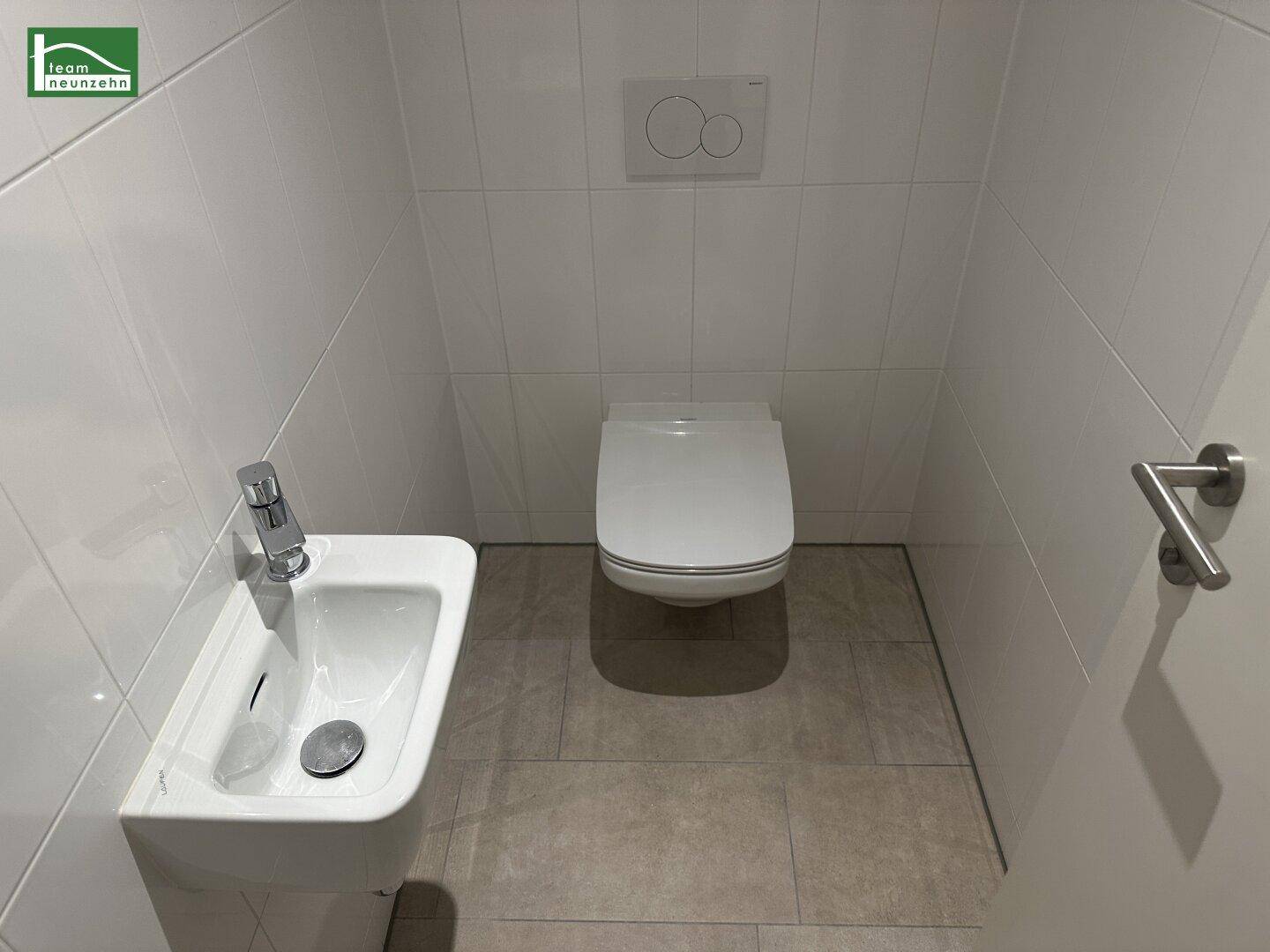 Kleines Gäste-WC mit wandhängender Toilette, kleinem Waschbecken und hellen Fliesen.