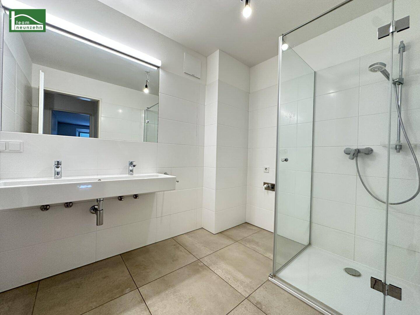 Modernes Badezimmer mit Doppelwaschbecken, großer Duschkabine und hellen Fliesen.