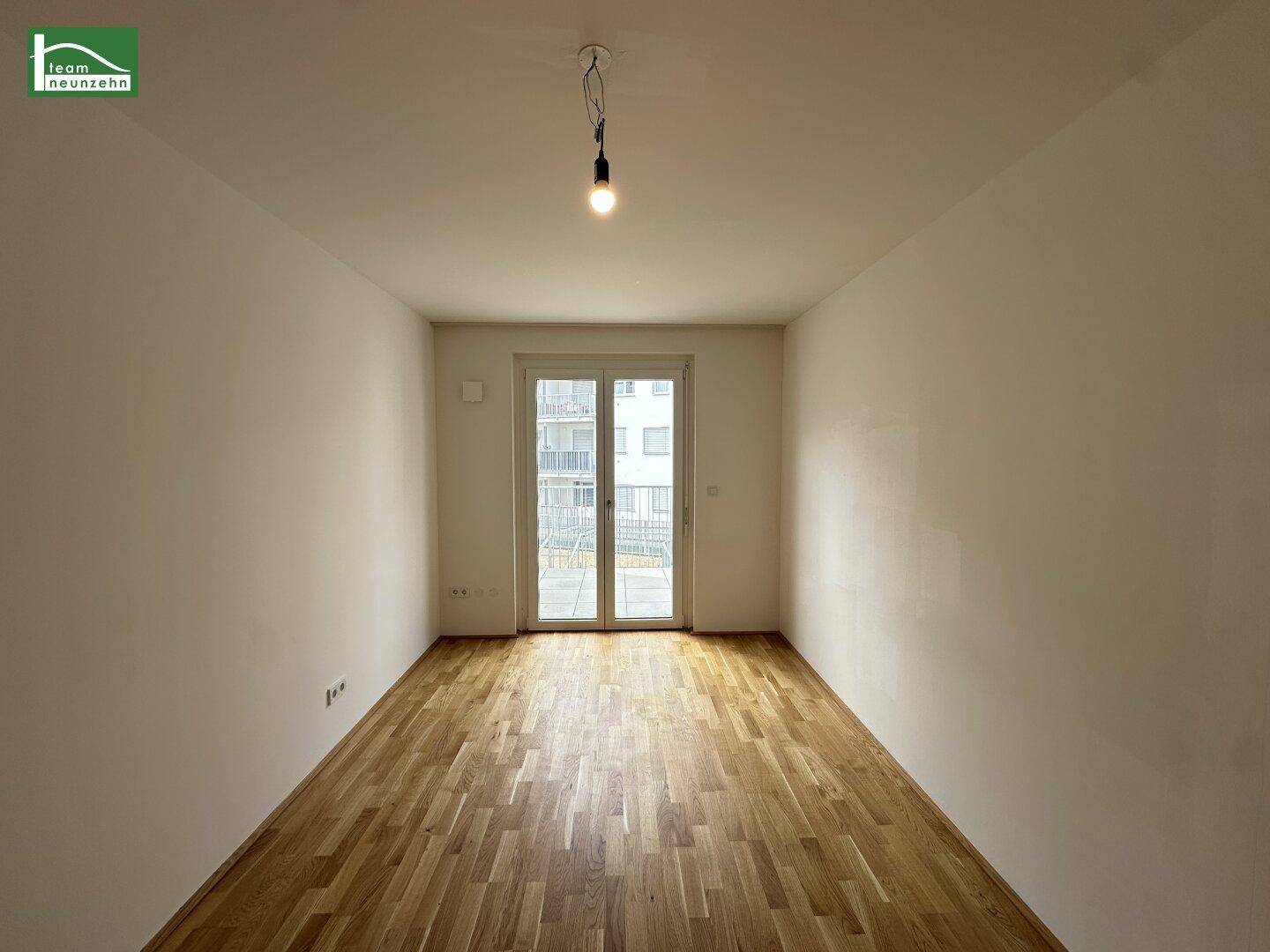 Geräumiger Wohnraum mit Parkettboden und großen Fenstern, die viel Licht hereinlassen.