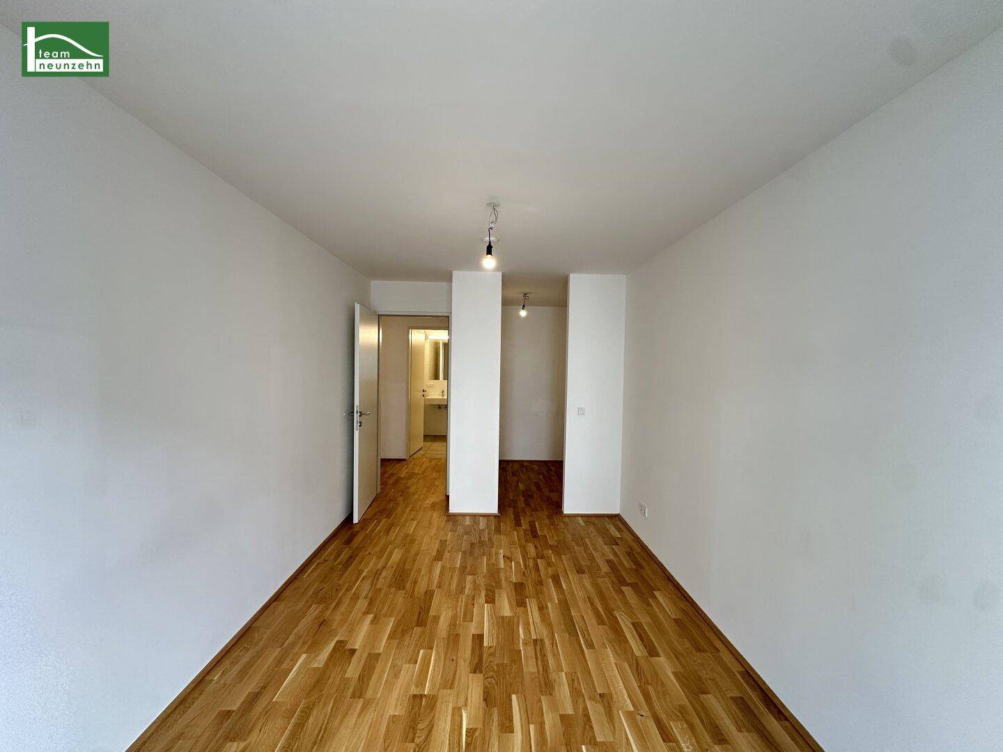 Heller Raum mit Parkettboden und Zugang zu einem modernen Badezimmer.