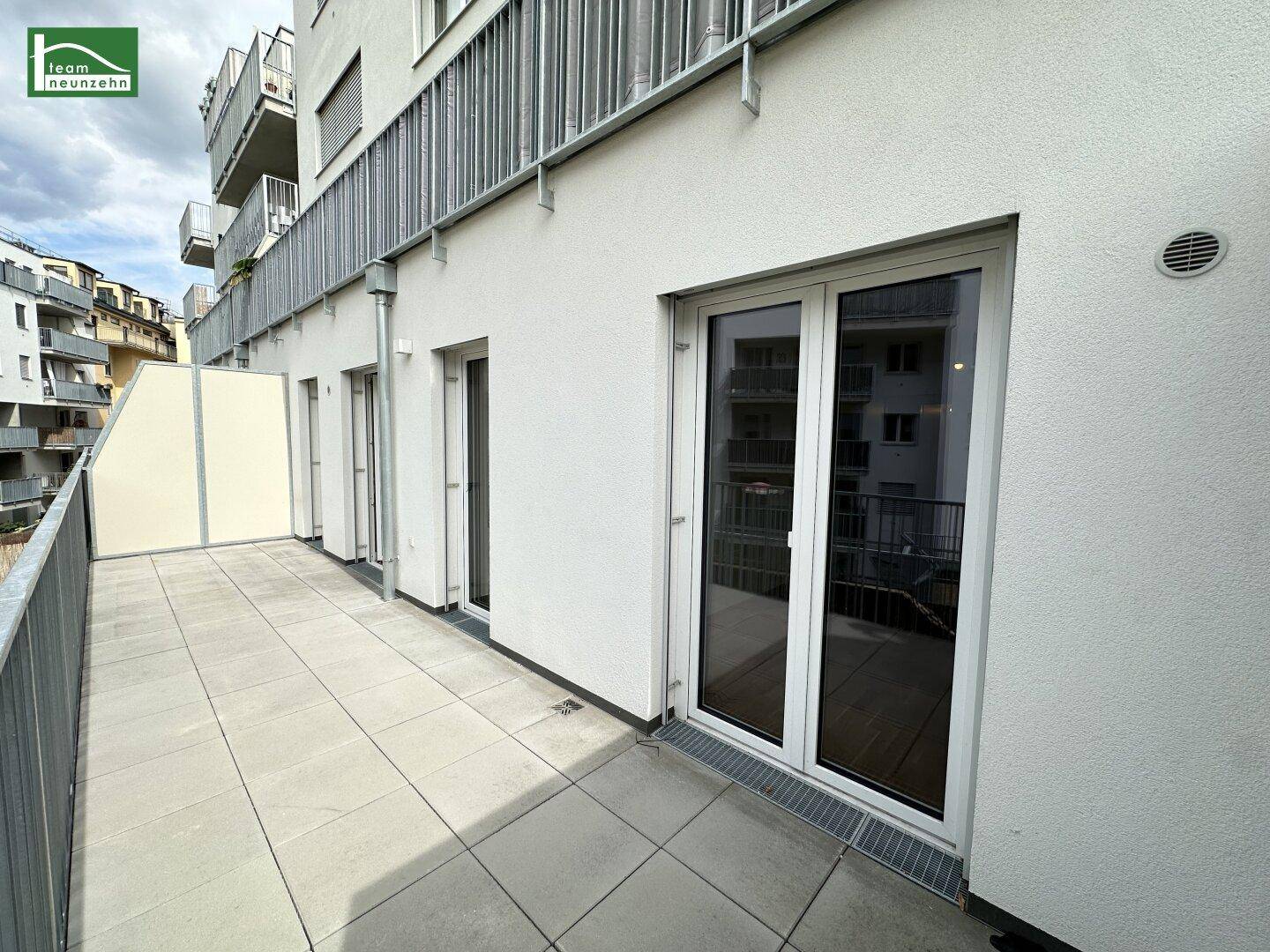 Balkon mit Fliesenboden und großen Glastüren, die in die Wohnung führen.