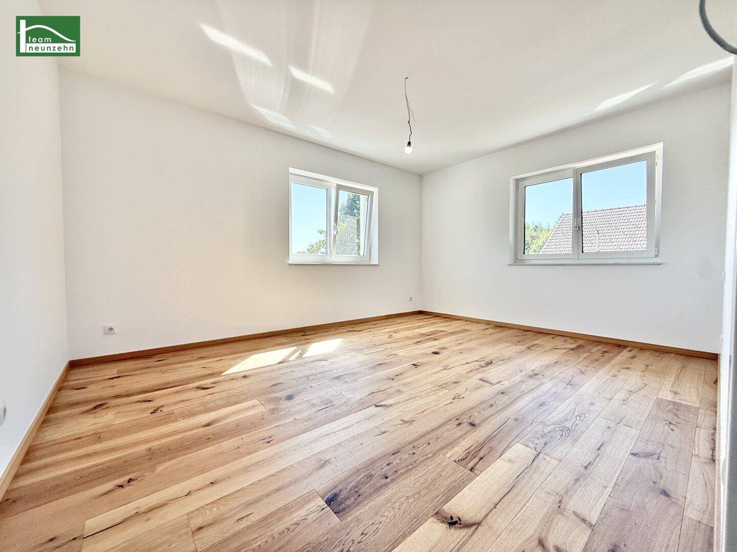 Geräumiges Schlafzimmer mit hellem Echtholzparkett und zwei Fenstern für viel Tageslicht.