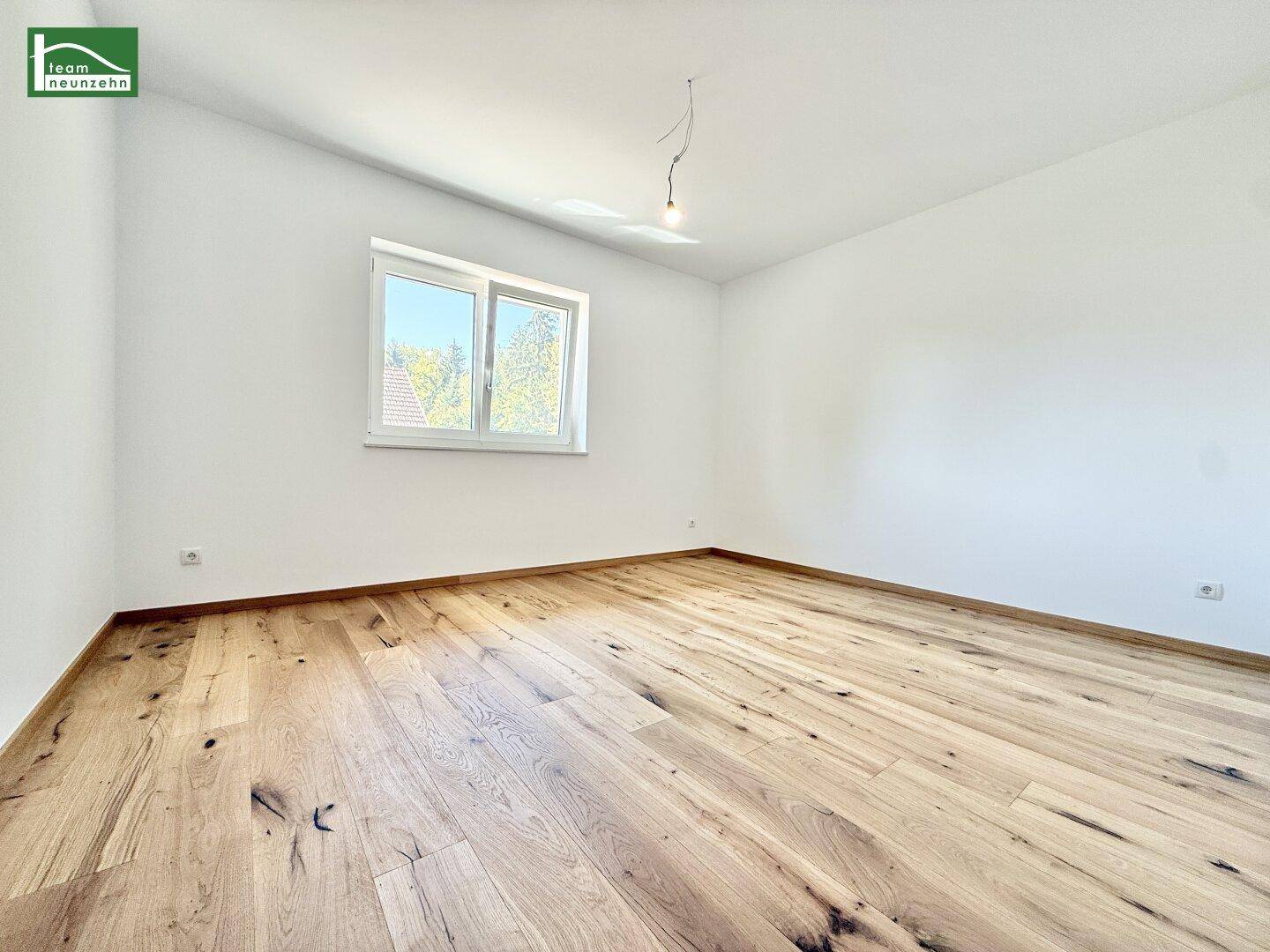 Lichtdurchflutetes Schlafzimmer mit Holzboden und einem großen Fenster mit Blick ins Grüne.