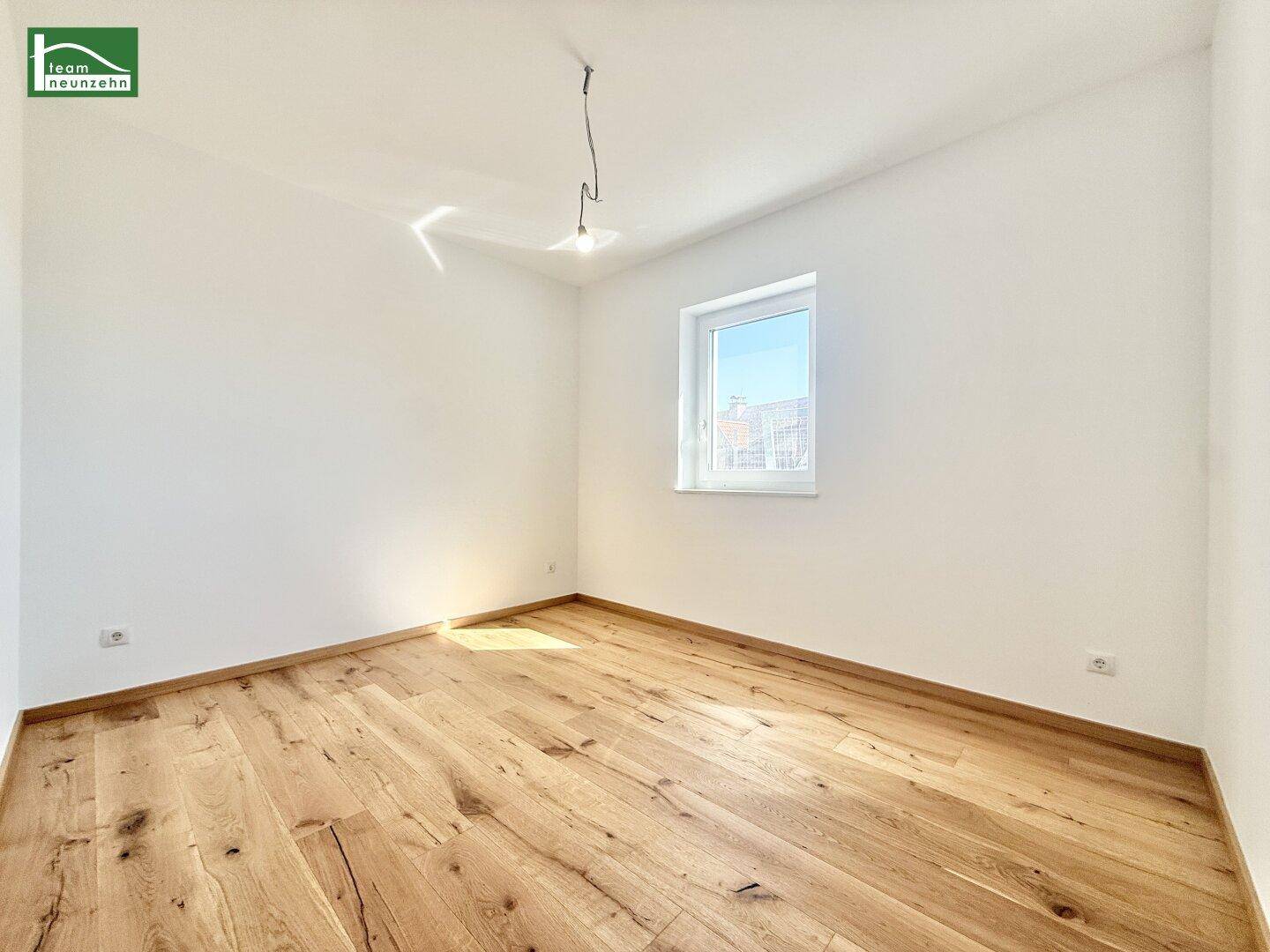 Lichtdurchflutetes Schlafzimmer mit Holzboden und einem Fenster, das viel Tageslicht hereinlässt.
