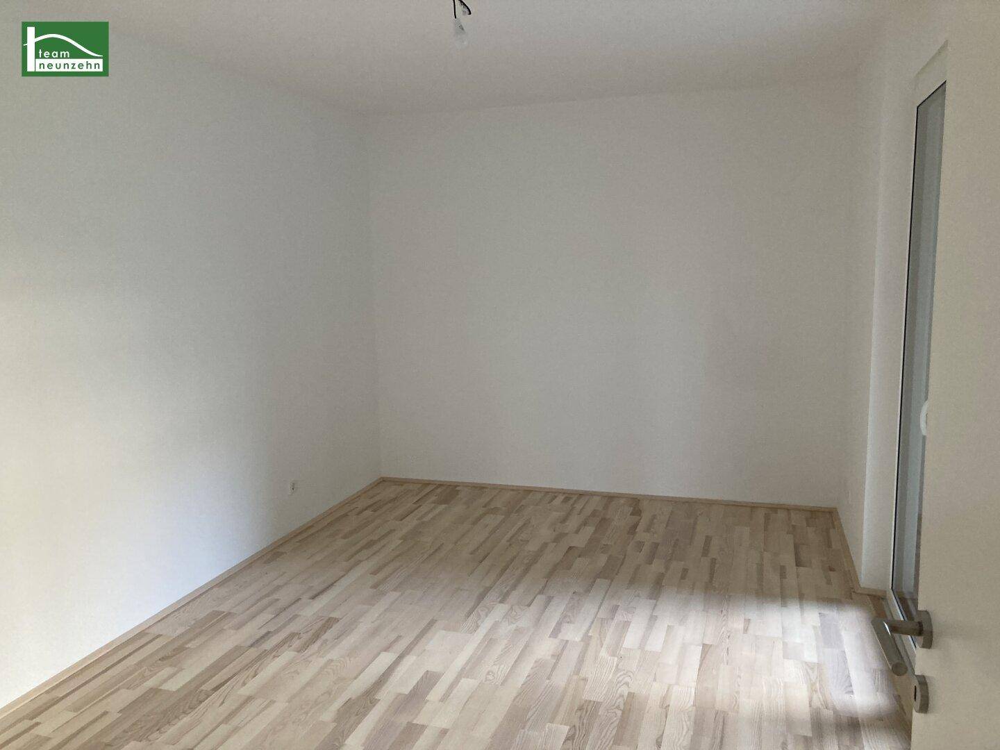 Leeres Schlafzimmer mit hellem Holzboden und Zugang zu einem Balkon oder einer Terrasse.