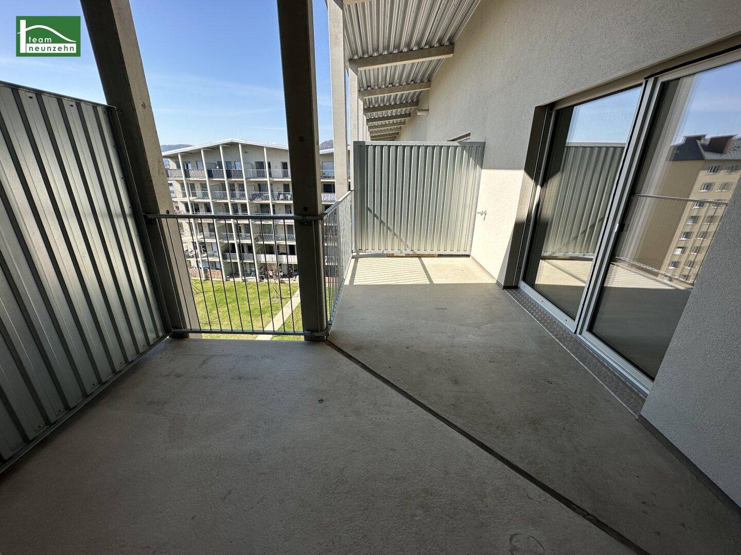 Geräumiger Balkon mit Betonboden und Metallgeländer, bietet einen Blick auf umliegende Gebäude.
