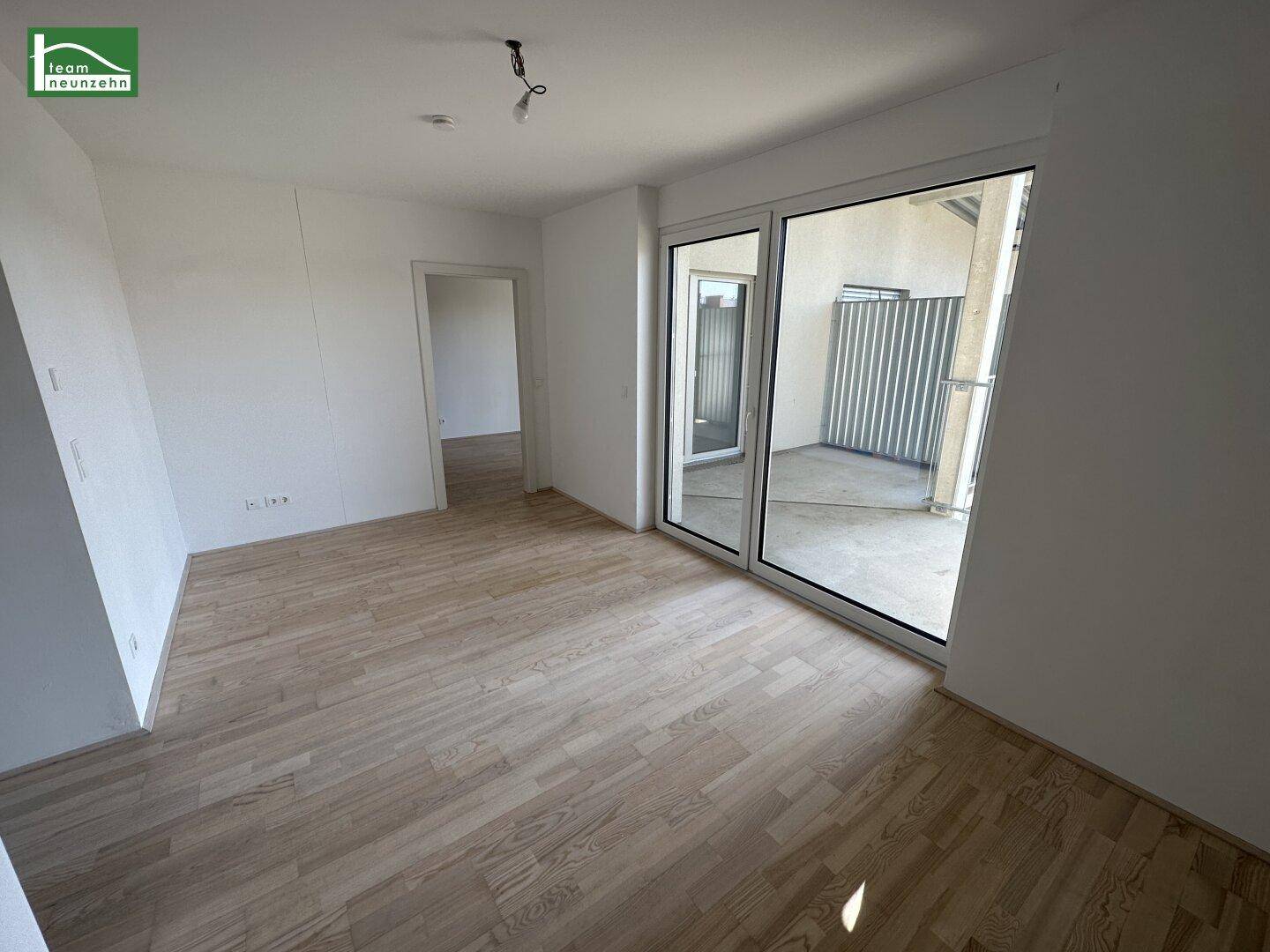Geräumiges, unmöbliertes Wohnzimmer mit Holzboden und großen Fenstern zum Balkon.