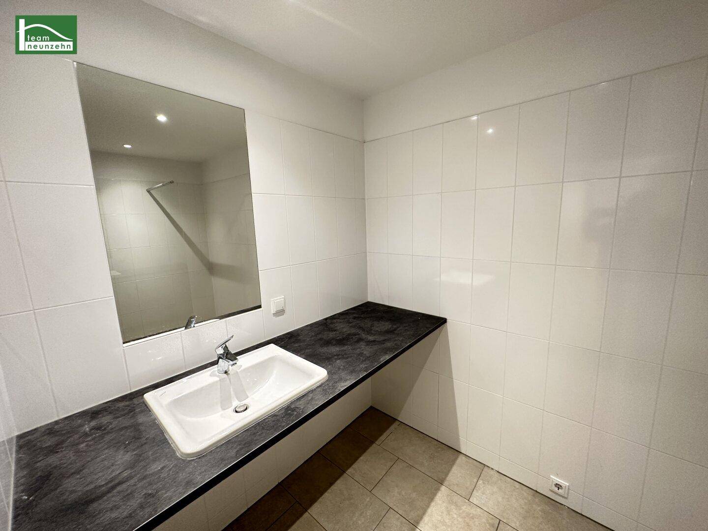 Modernes Badezimmer mit weißen Fliesen, dunkler Waschtischplatte und großem Spiegel.