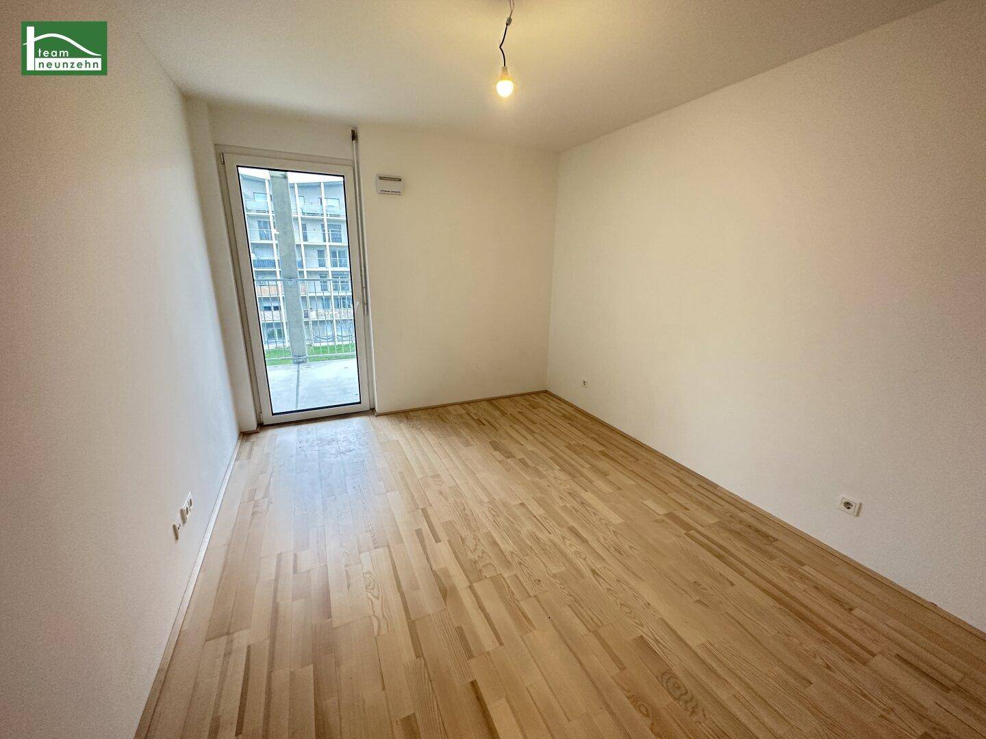 Helles, leeres Schlafzimmer mit Parkettboden und Zugang zu einem Außenbereich.