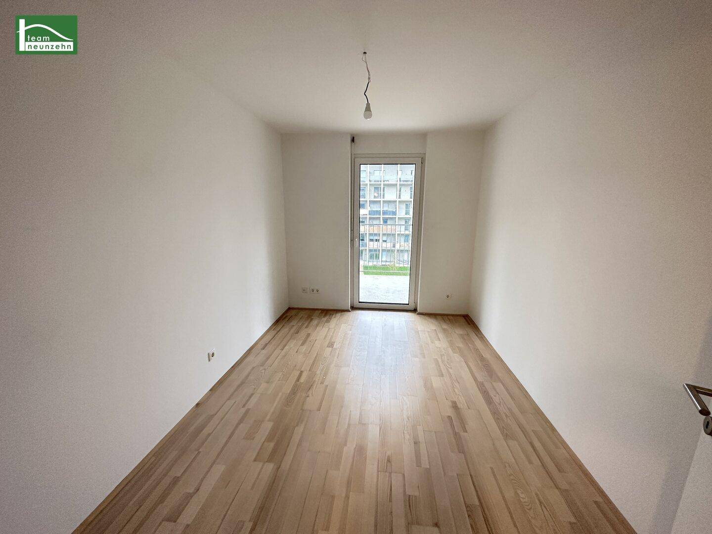 Geräumiges, unmöbliertes Zimmer mit hellem Parkettboden und viel Tageslicht.