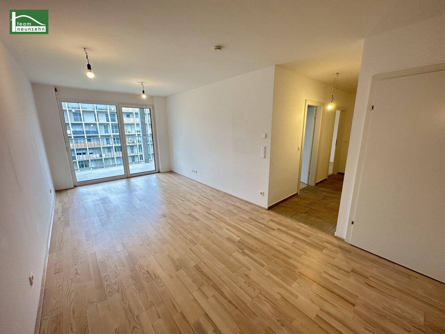 Heller, leerer Wohn-Essbereich mit Holzboden und Zugang zu einem Balkon oder einer Terrasse.