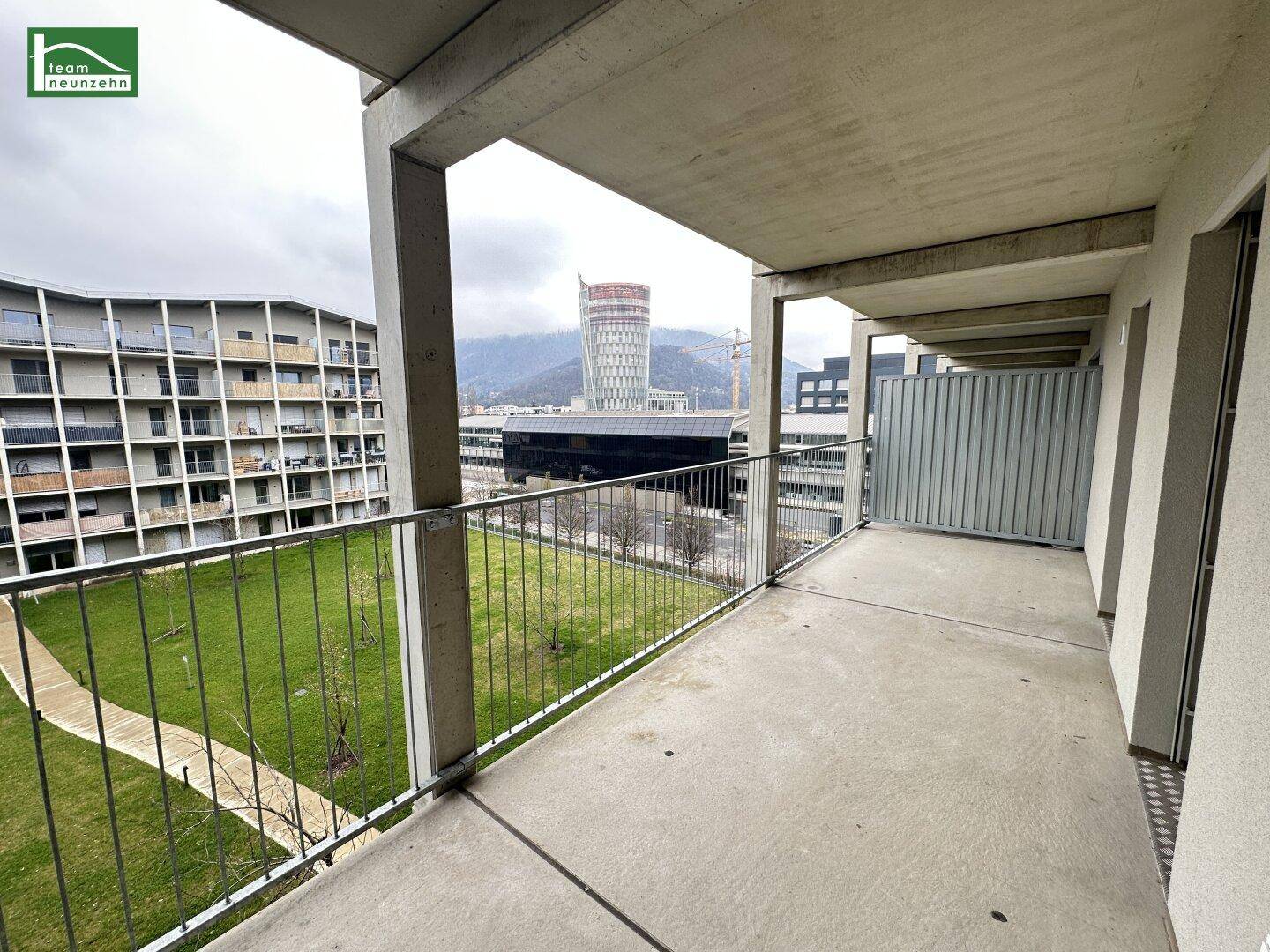 Geräumiger Betonbalkon mit Metallgeländer und Blick auf den grünen Innenhof und die Stadt.