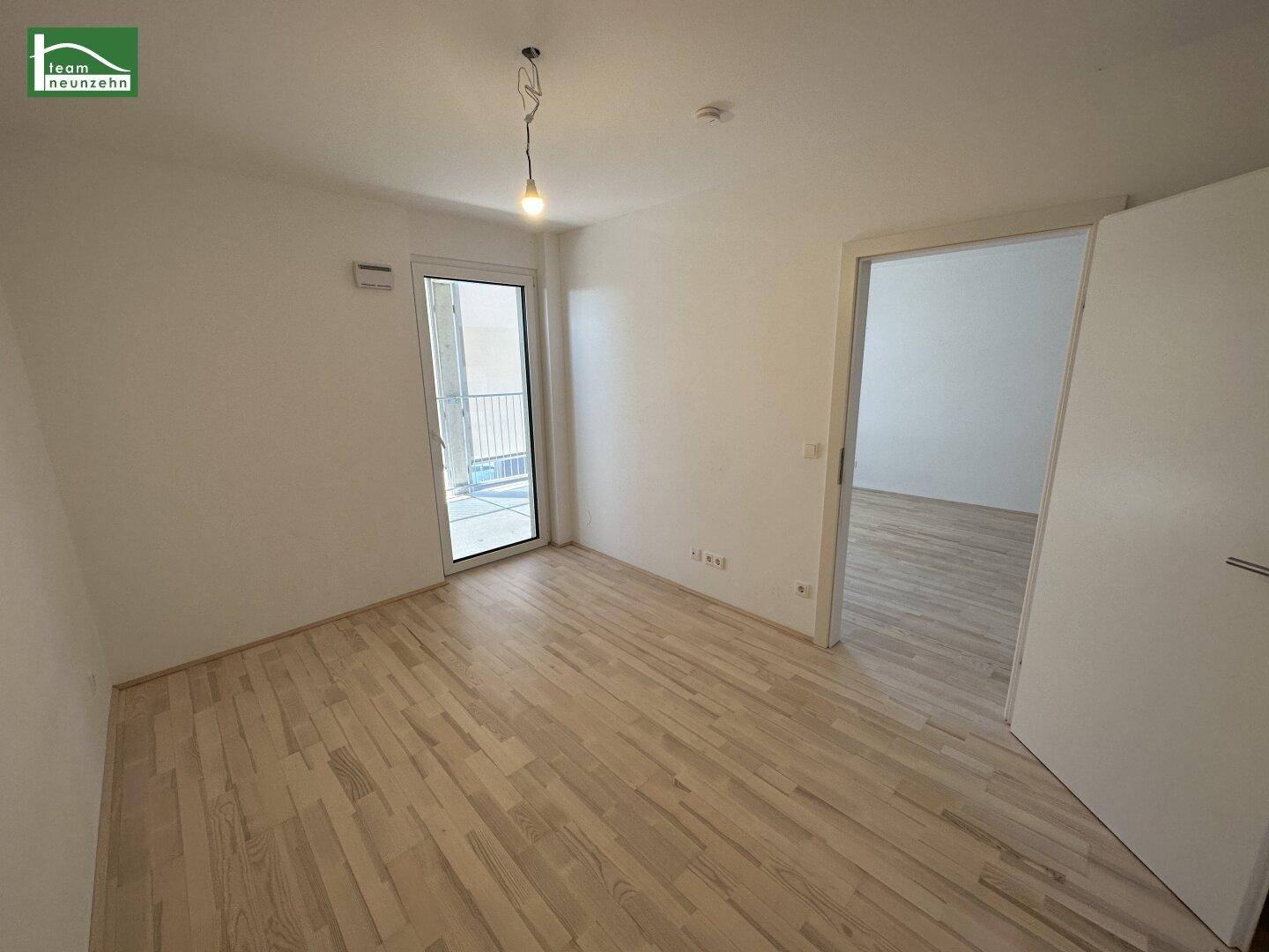 Helles, leeres Zimmer mit Parkettboden und Zugang zu einem Balkon, bereit zur Einrichtung.