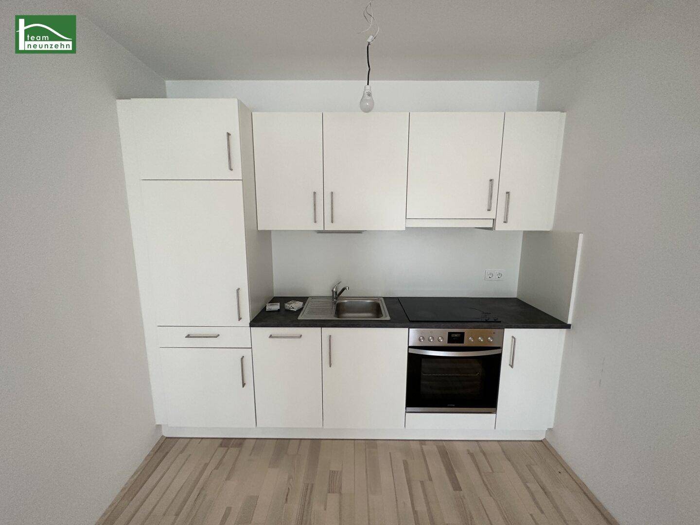 Kompakte, weiße Küchenzeile mit integriertem Backofen und Spüle in einem modernen Wohnraum.