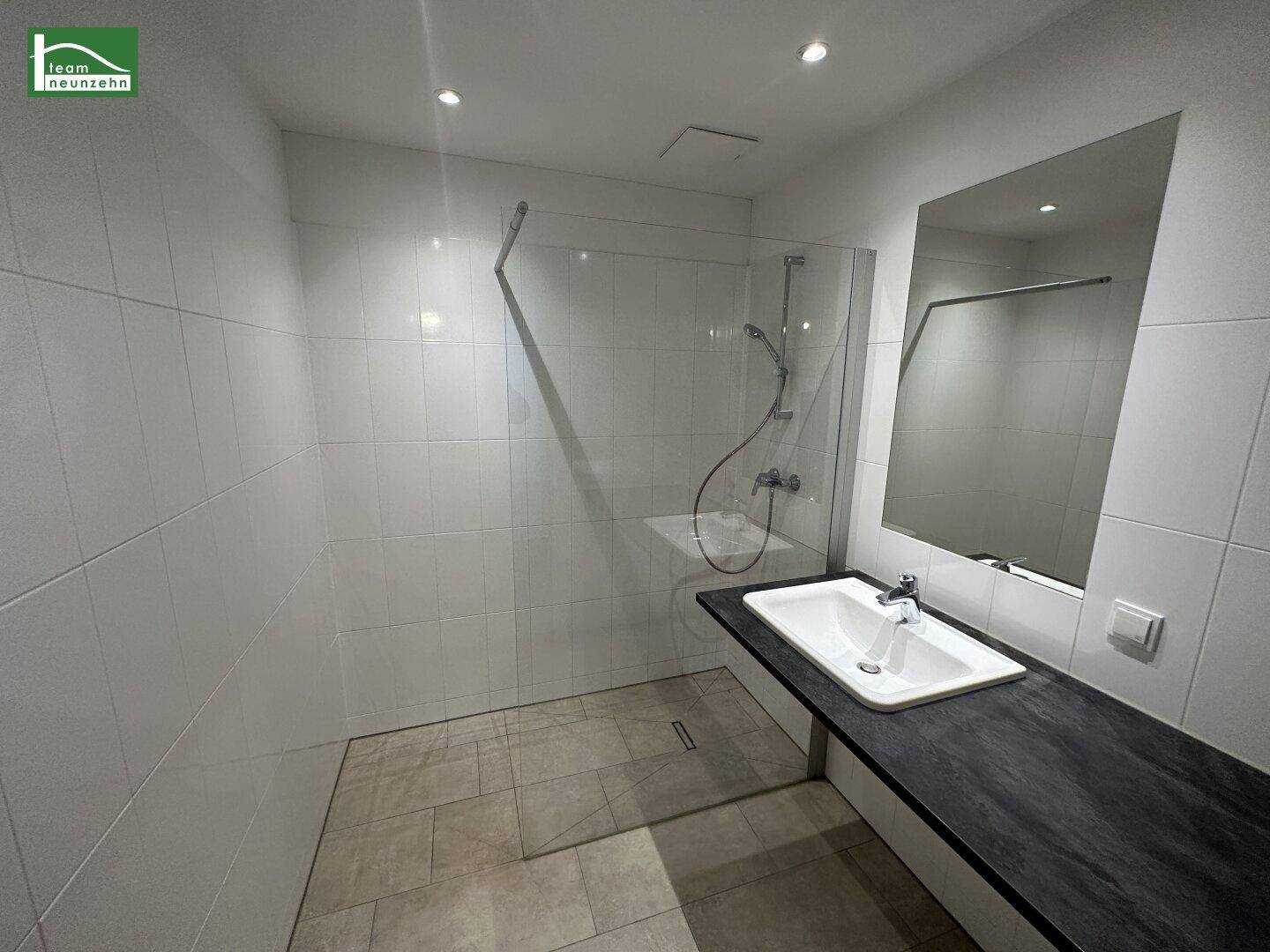 Modernes Badezimmer mit weiß gefliesten Wänden, ebenerdiger Dusche und großem Waschbecken.