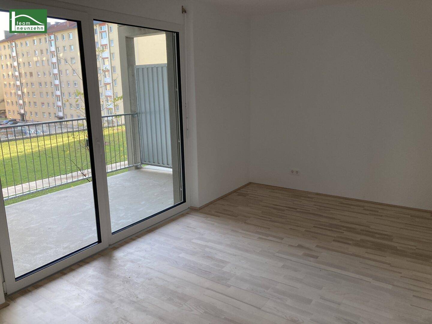 Heller, leerer Raum mit hellem Parkettboden und großen Schiebetüren zum Balkon.