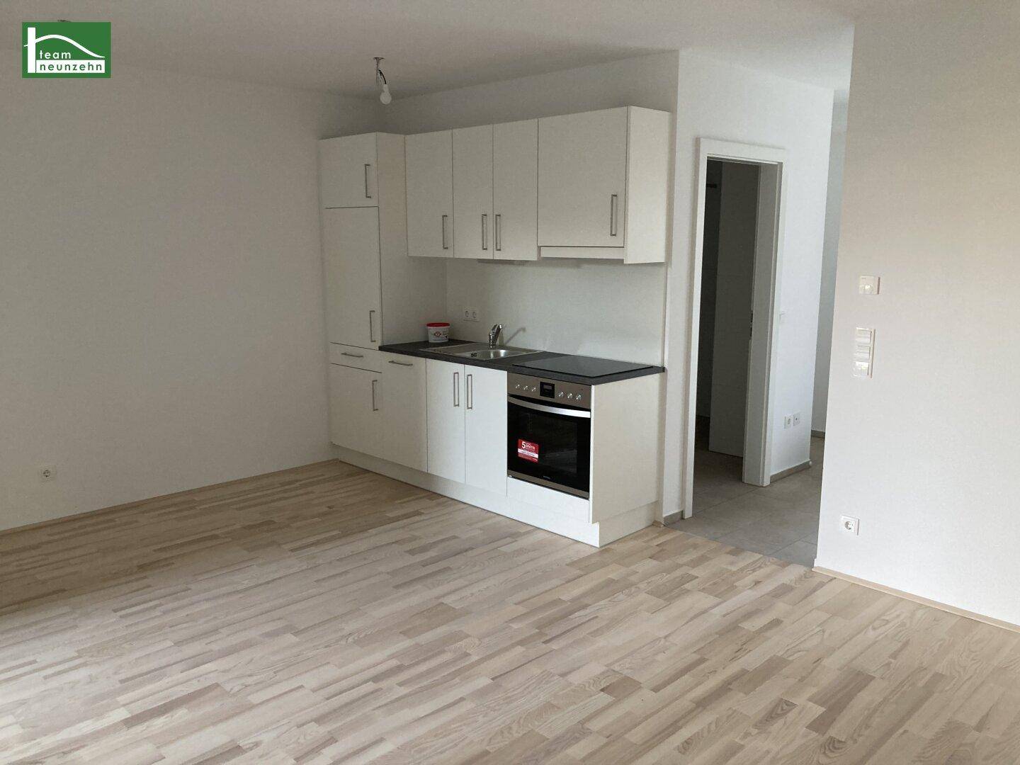 Kleine, funktionale Küchenzeile mit weißen Schränken und integriertem Backofen in einem hellen Raum.