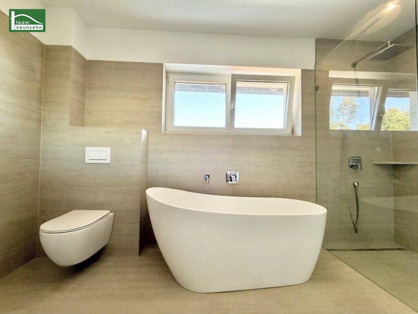 Helles Badezimmer mit freistehender Badewanne, wandhängendem WC und Fenster für Tageslicht.