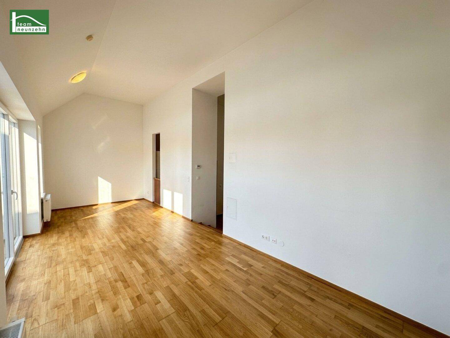 Geräumiges, helles Wohnzimmer mit Holzboden und viel Tageslicht durch große Fenster.