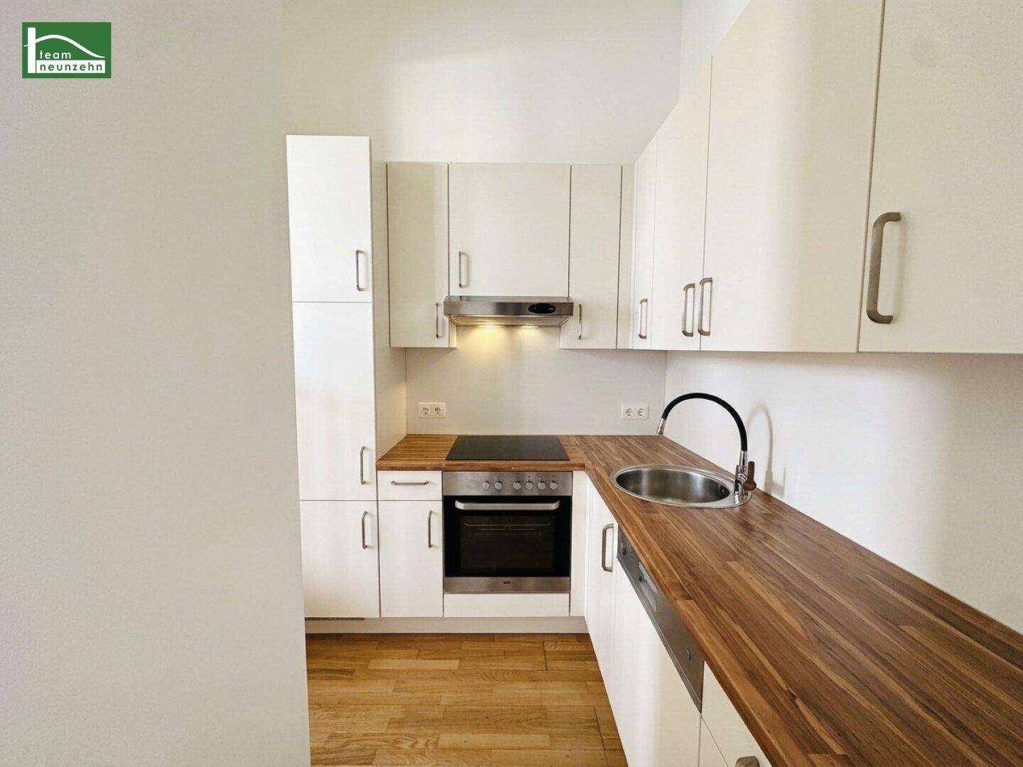 Moderne Einbauküche mit weißen Schränken, Holz-Arbeitsplatte und integrierten Elektrogeräten.
