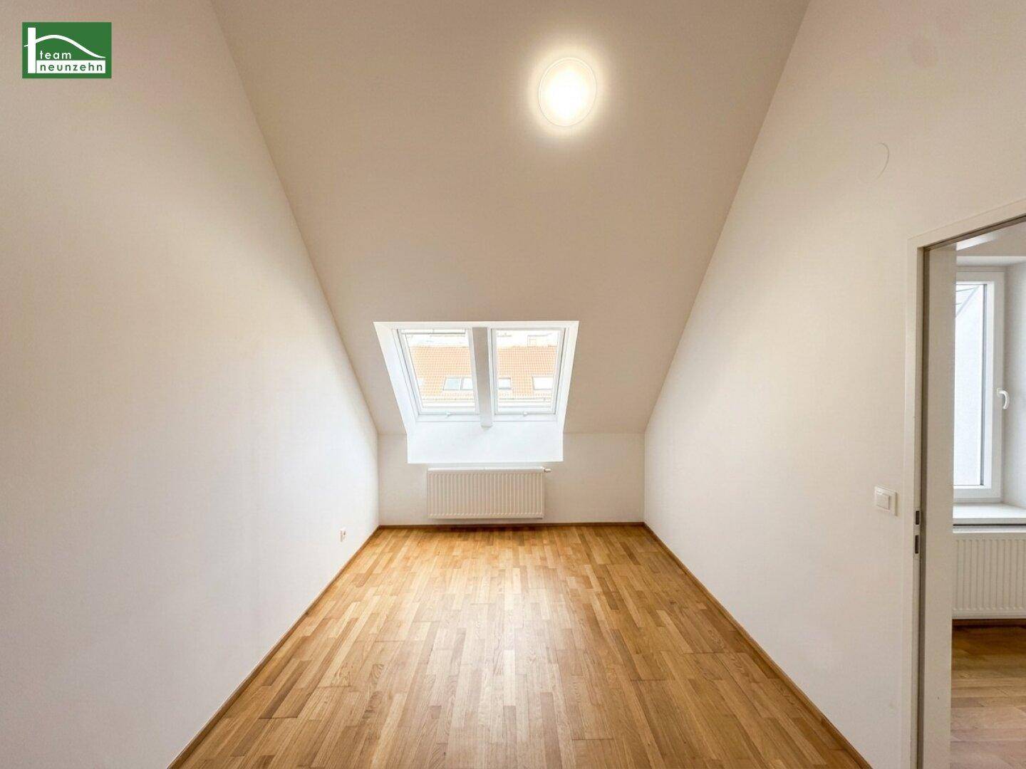 Helles Dachgeschosszimmer mit schrägen Wänden, Holzboden und Dachfenster für viel Tageslicht.