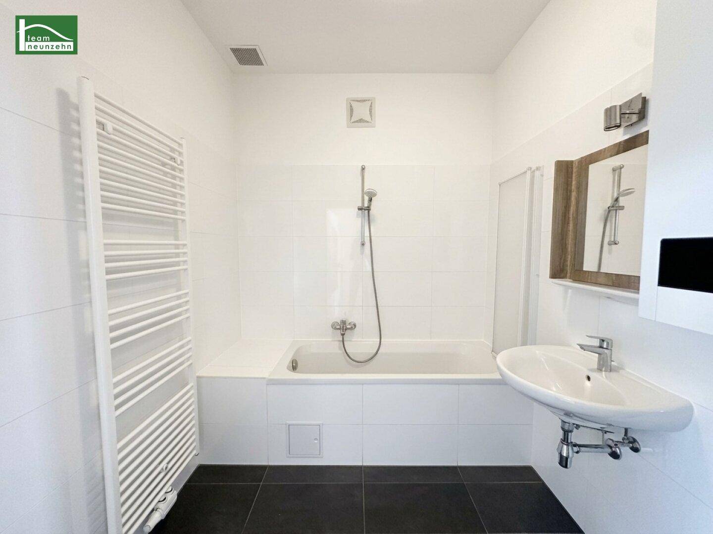 Modernes Badezimmer mit Badewanne, Waschbecken, weißen Fliesen und beheiztem Handtuchhalter.